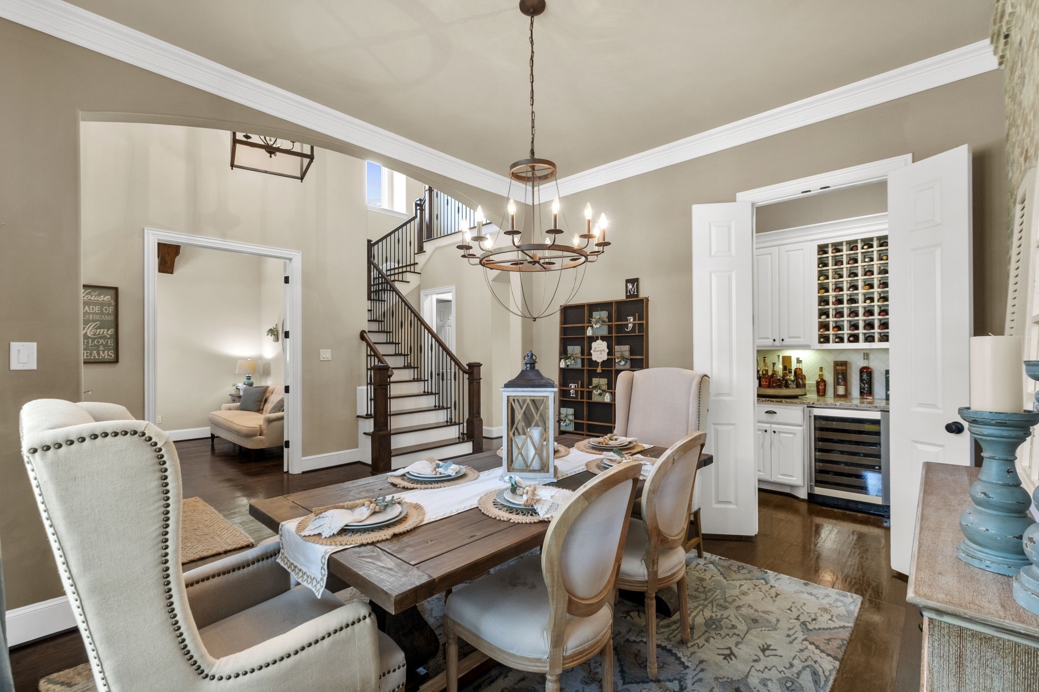 View from the formal dining room showing its open flow into the foyer, direct access to the dry bar area through double folding doors, and high ceiling with crown molding details.