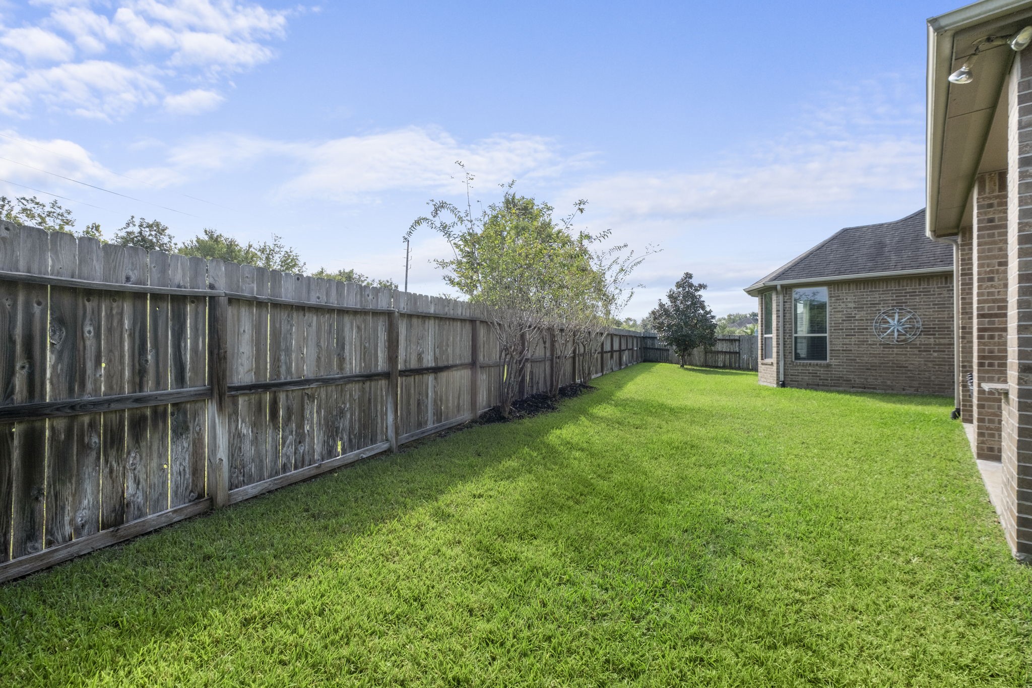 Expansive side yard featuring lush green lawn and an extensive wood privacy fence with mature boundary plantings running along the property line.
