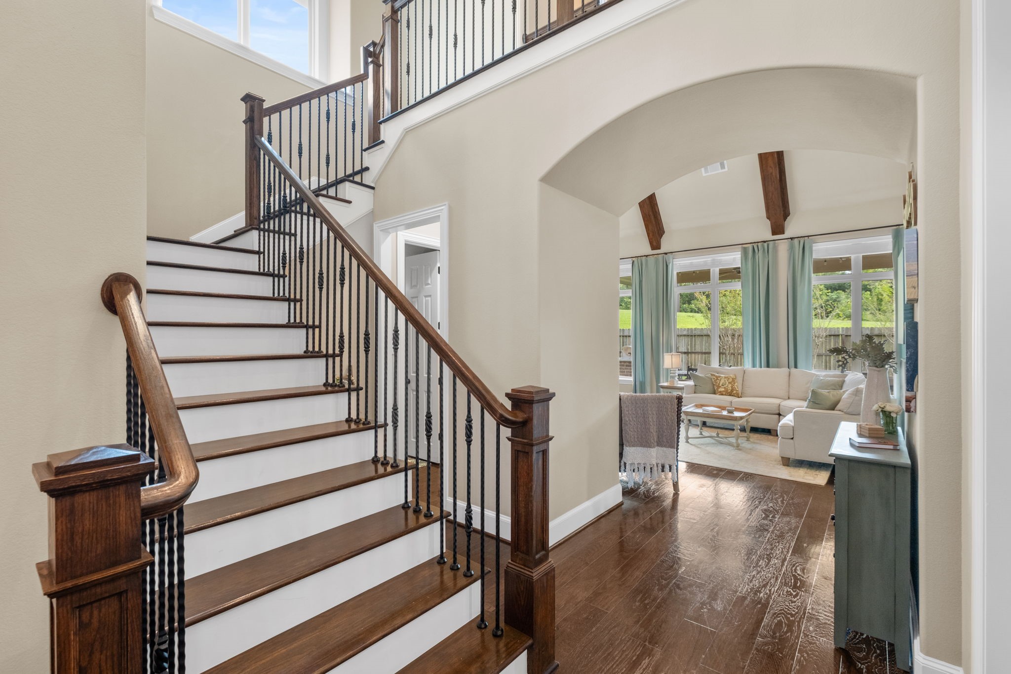 Dramatic entry stairwell featuring rich hardwood treads, painted white risers, and a wrought-iron decorative balustrade. An elegant architectural archway opens into the main living room, highlighting the home's open-concept layout and continuous hardwood flooring.