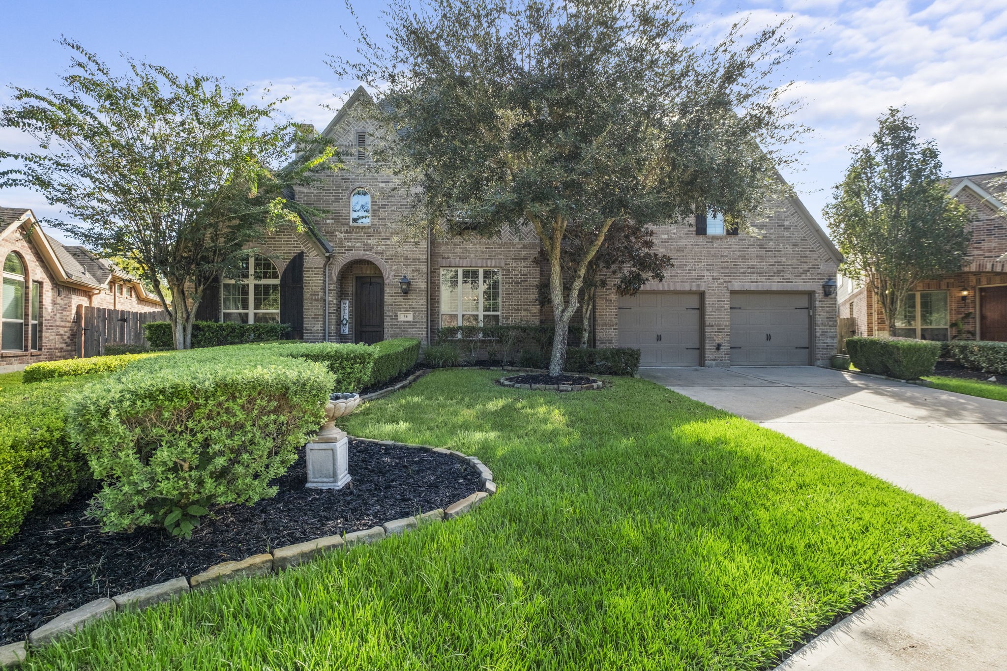 Expansive front lawn highlighting professional landscaping with sculpted boxwood hedges, mature shade trees, and a decorative stone fountain centerpiece set in black mulch beds.