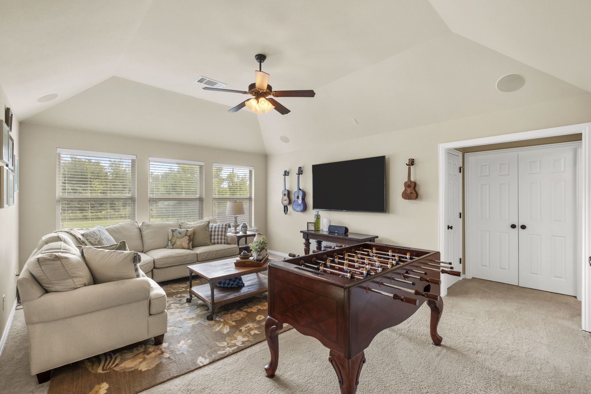 Expansive upstairs game room or media space boasting vaulted ceilings, integrated ceiling speakers, a ceiling fan, plush carpeting, and three large double-hung windows providing elevated natural lighting. Includes a walk-in storage closet.