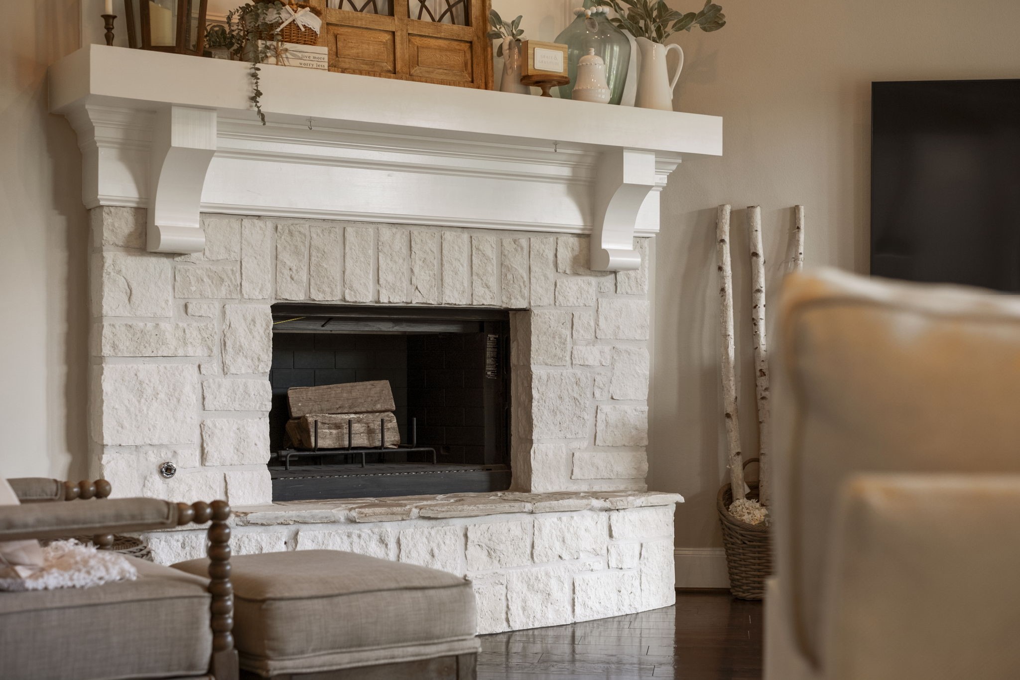 Close-up architectural detail of the main living area fireplace, showcasing light-colored natural cut-stone masonry, a raised hearth stone bench, and a substantial painted wood mantle with decorative support corbels.