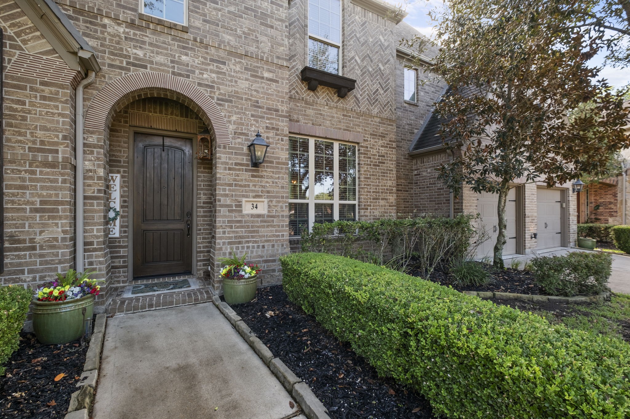 Covered stone entry archway boasting a custom solid wood front door with a glass accent window. Detailed with brick herringbone accents, a charming window flower box, and custom stone address plaque.