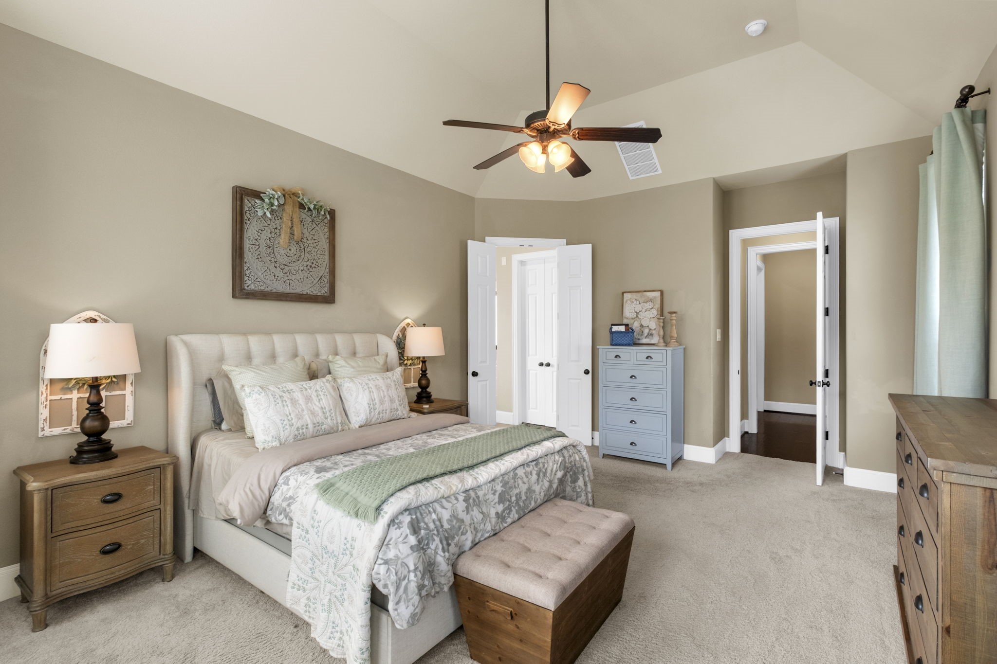 Alternate view of the primary bedroom showing the expansive floor plan, tray ceiling design, neutral wall color, and double doors leading into the ensuite primary bathroom.