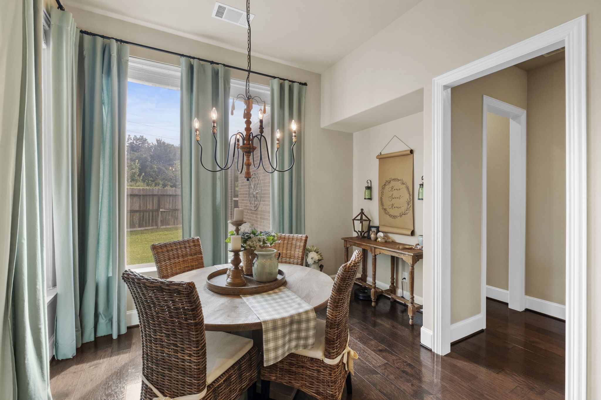 Light-filled breakfast room featuring large picture windows with yard views, a decorative chandelier lighting mount, warm hardwood floors, and direct access through a wide trim case opening to the surrounding common areas.