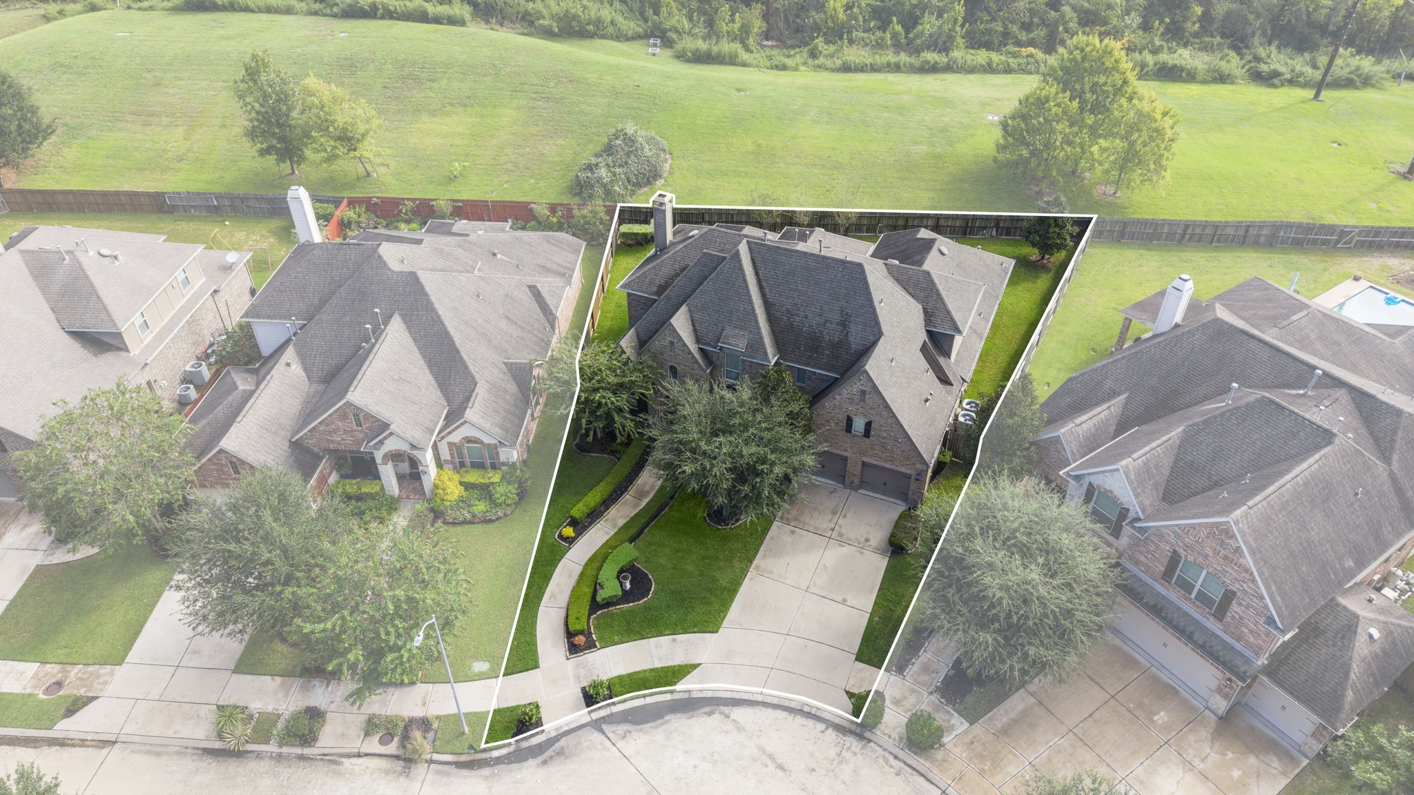 Elevated front-facing aerial photo outlining the property boundaries, deep concrete multi-car driveway, curated front yard landscaping, mature shade trees, and stone exterior finish.