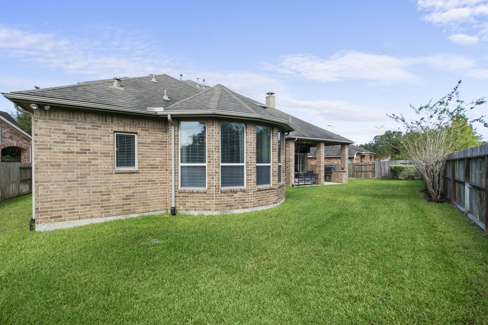 Rear perspective showcasing the architectural brick exterior with a prominent multi-window bay bump-out, gutters, and expansive green lawn enclosed by a wood privacy fence.