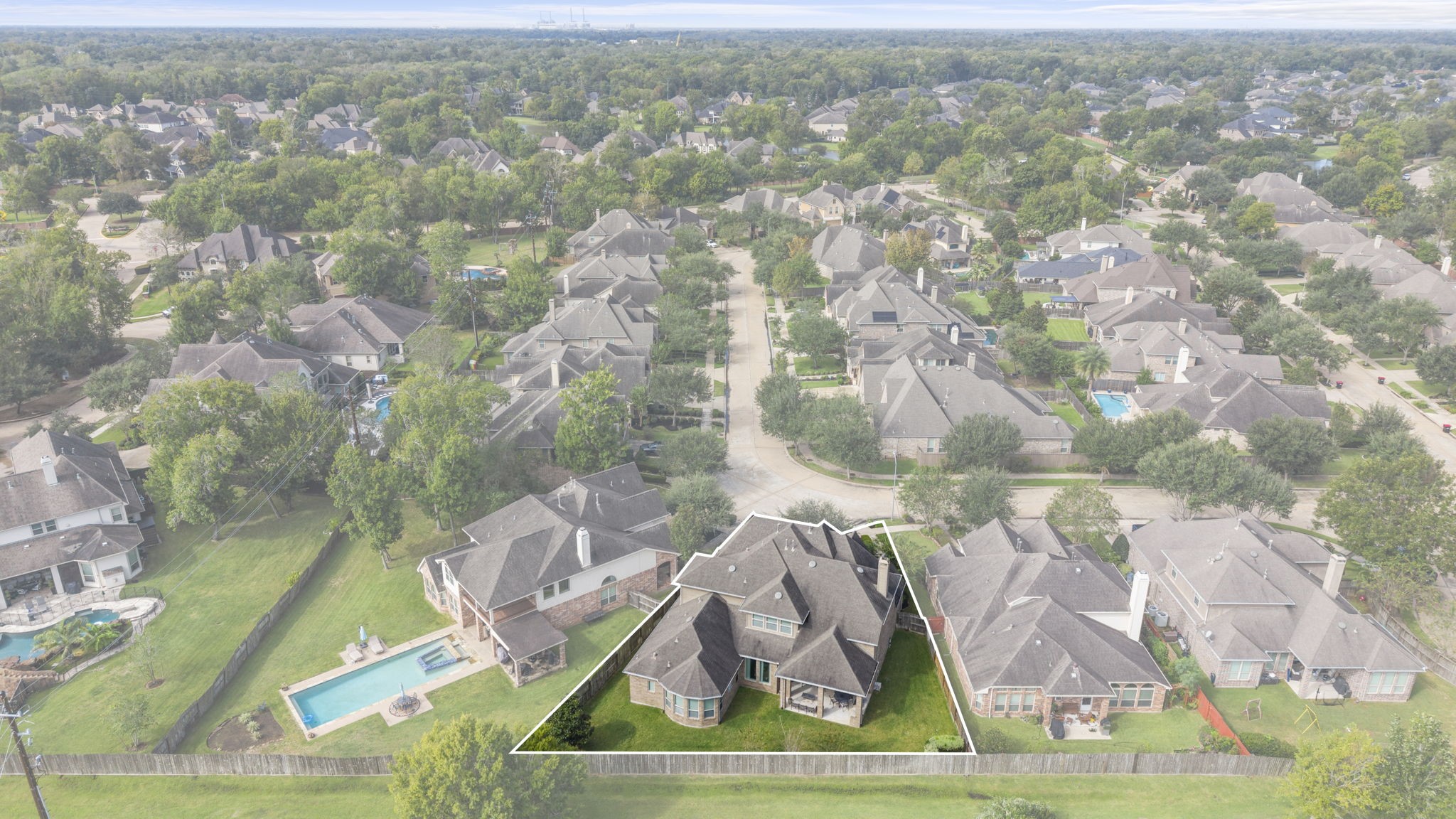 Wide aerial photograph showing the surrounding residential community, tree-lined neighborhood streets, mature canopy, and proximity to neighboring green spaces.