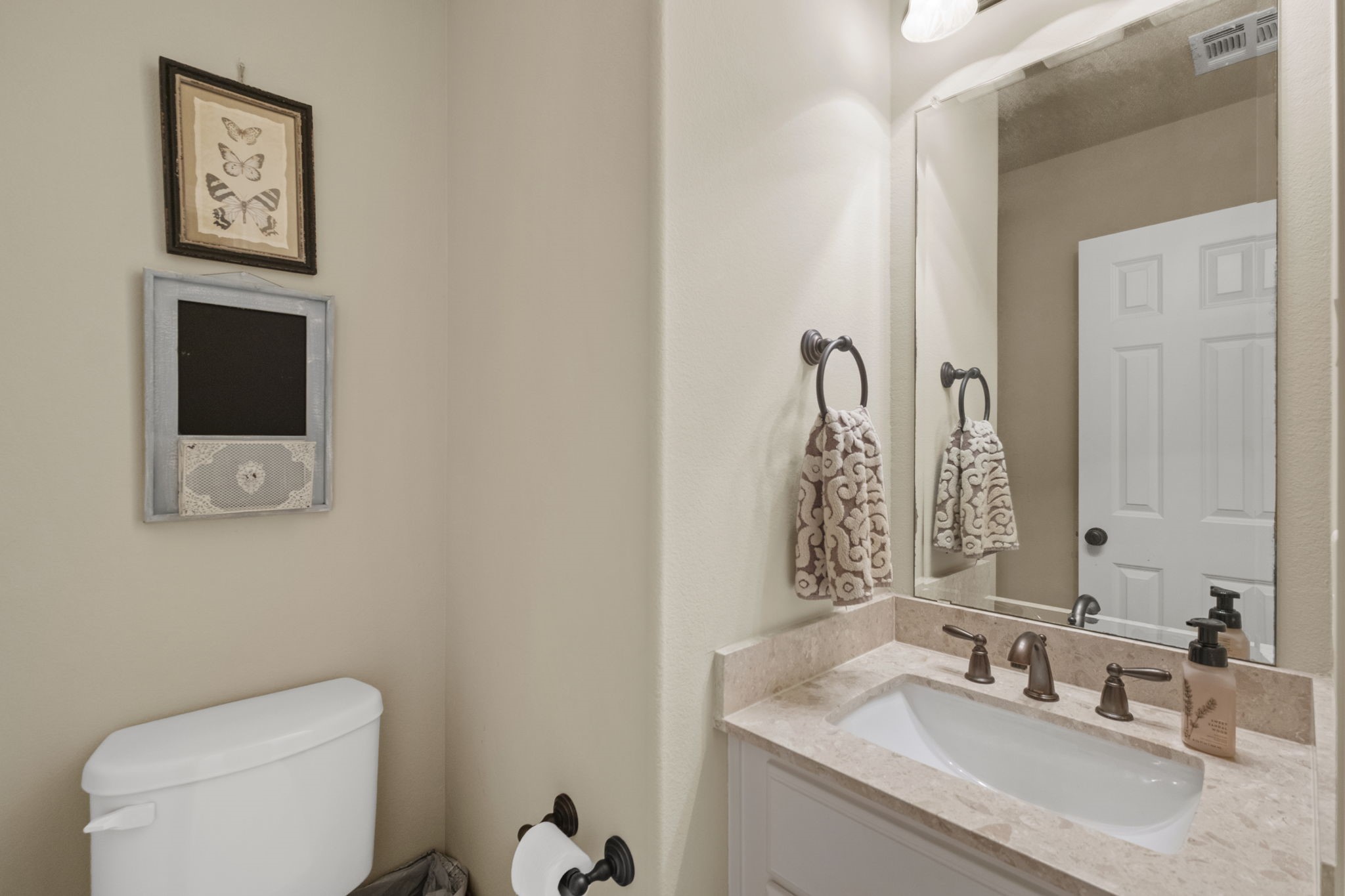 Upstairs guest half-bath featuring a vanity with a light stone countertop, oil-rubbed bronze faucet and hardware, large frameless wall mirror, neutral wall paint, and toilet alcove.