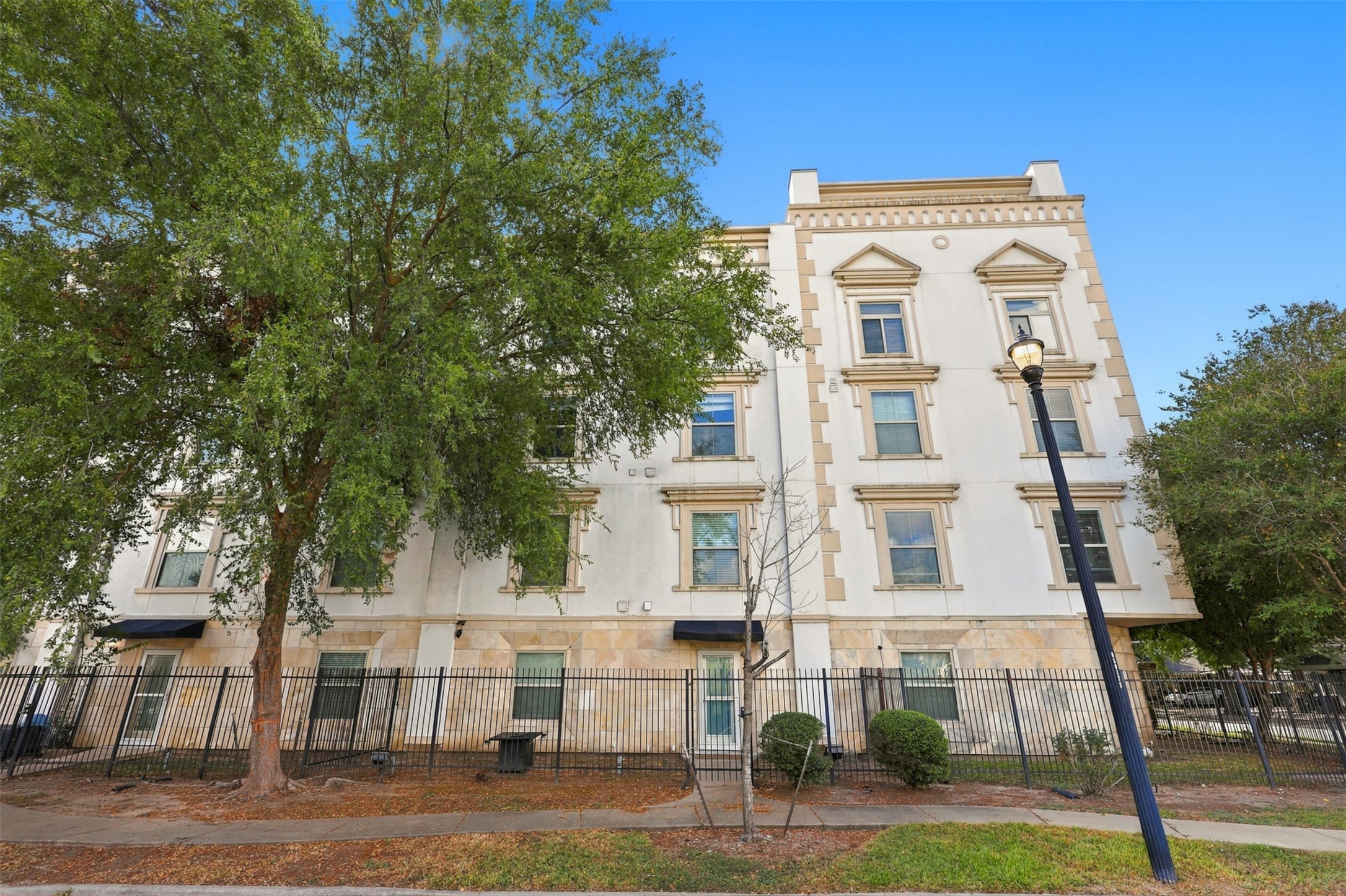 Elegant four-story building with classic architectural details, complemented by lush greenery and a secure fenced perimeter.