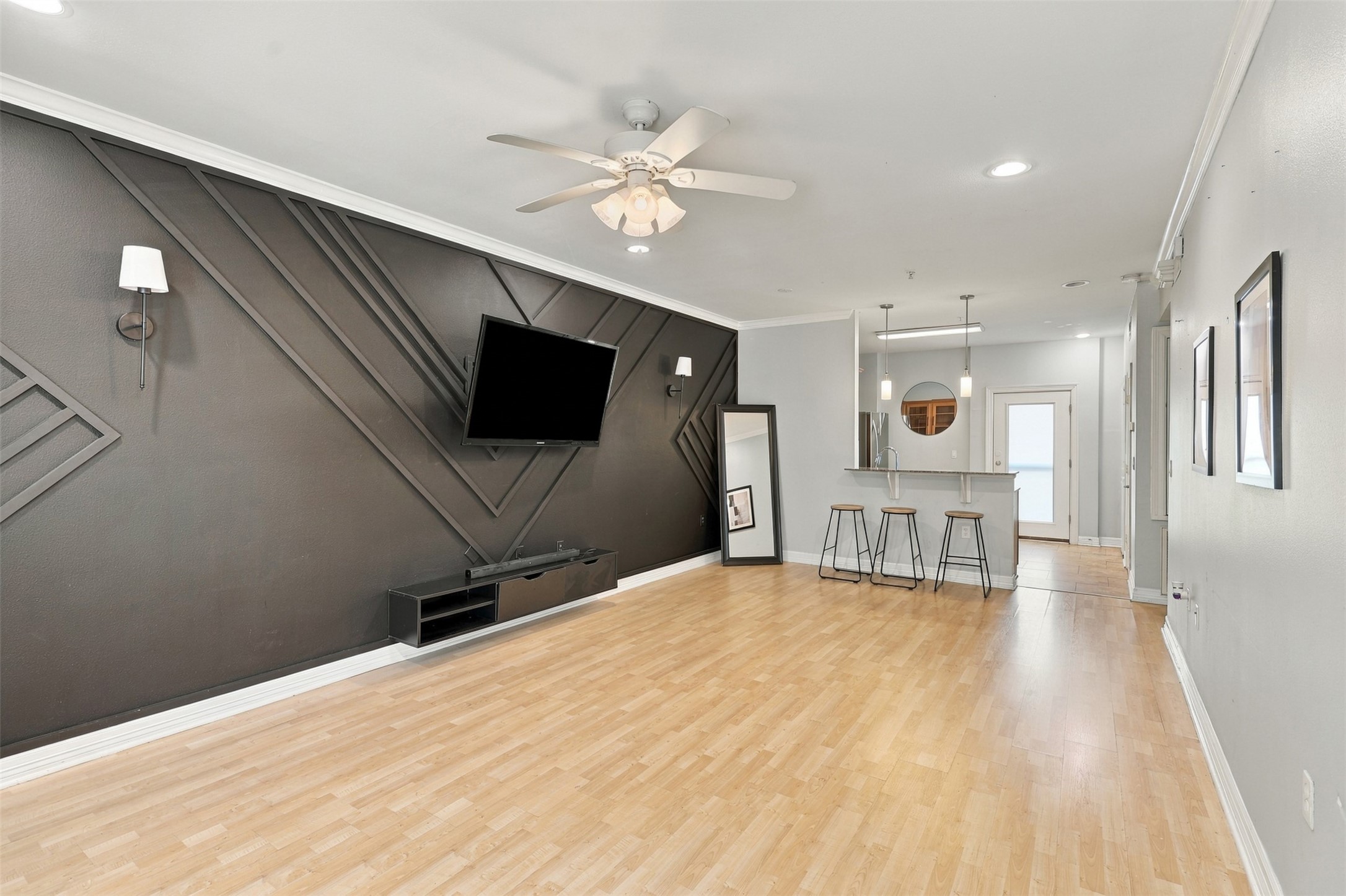 Chic living area with modern geometric accent wall, ceiling fan, and open layout leading to a cozy breakfast bar and kitchen.