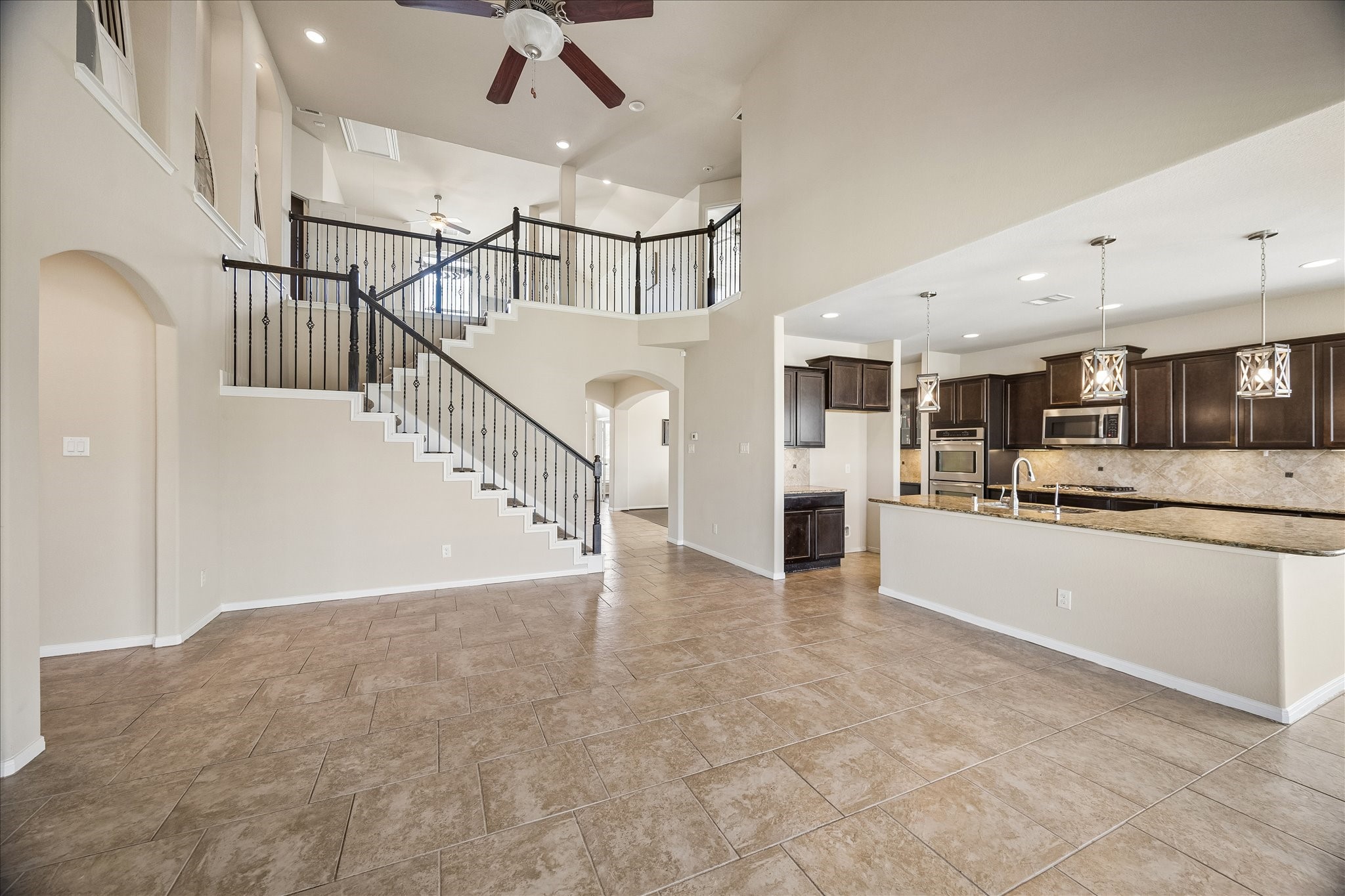 The spacious living room features high ceilings, a striking staircase with wrought-iron balusters, and beautiful tile flooring.