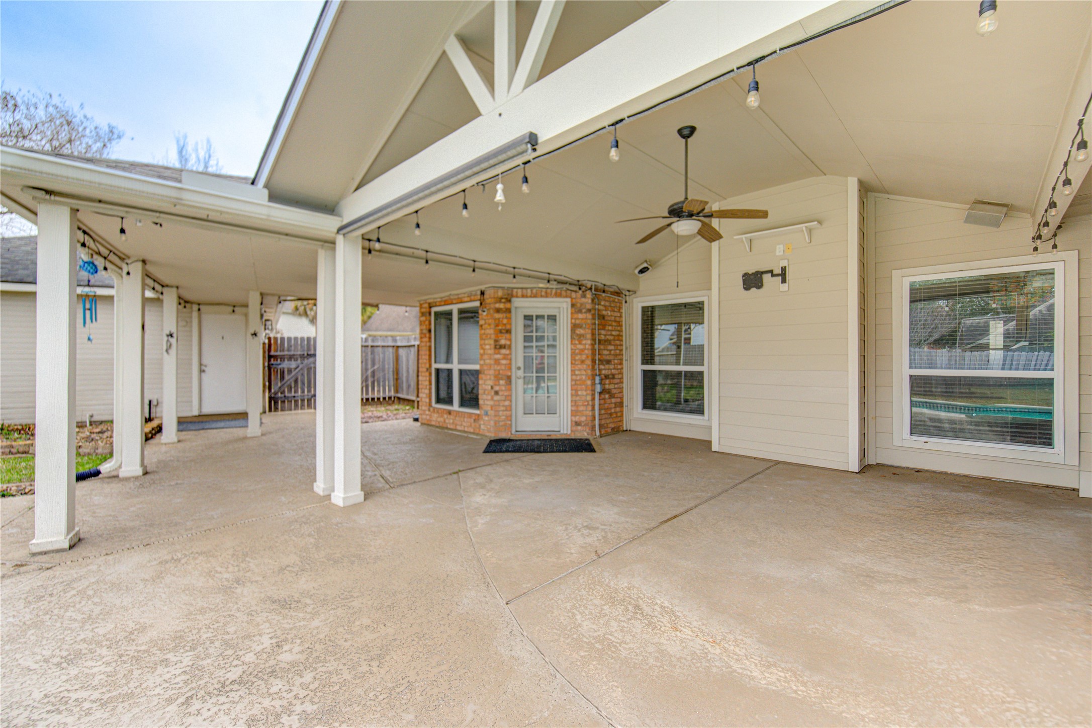 This spacious covered patio with a ceiling fan and string lights, TV wall mount, semi sheer outdoor roller shade  ideal for outdoor relaxation and entertaining.