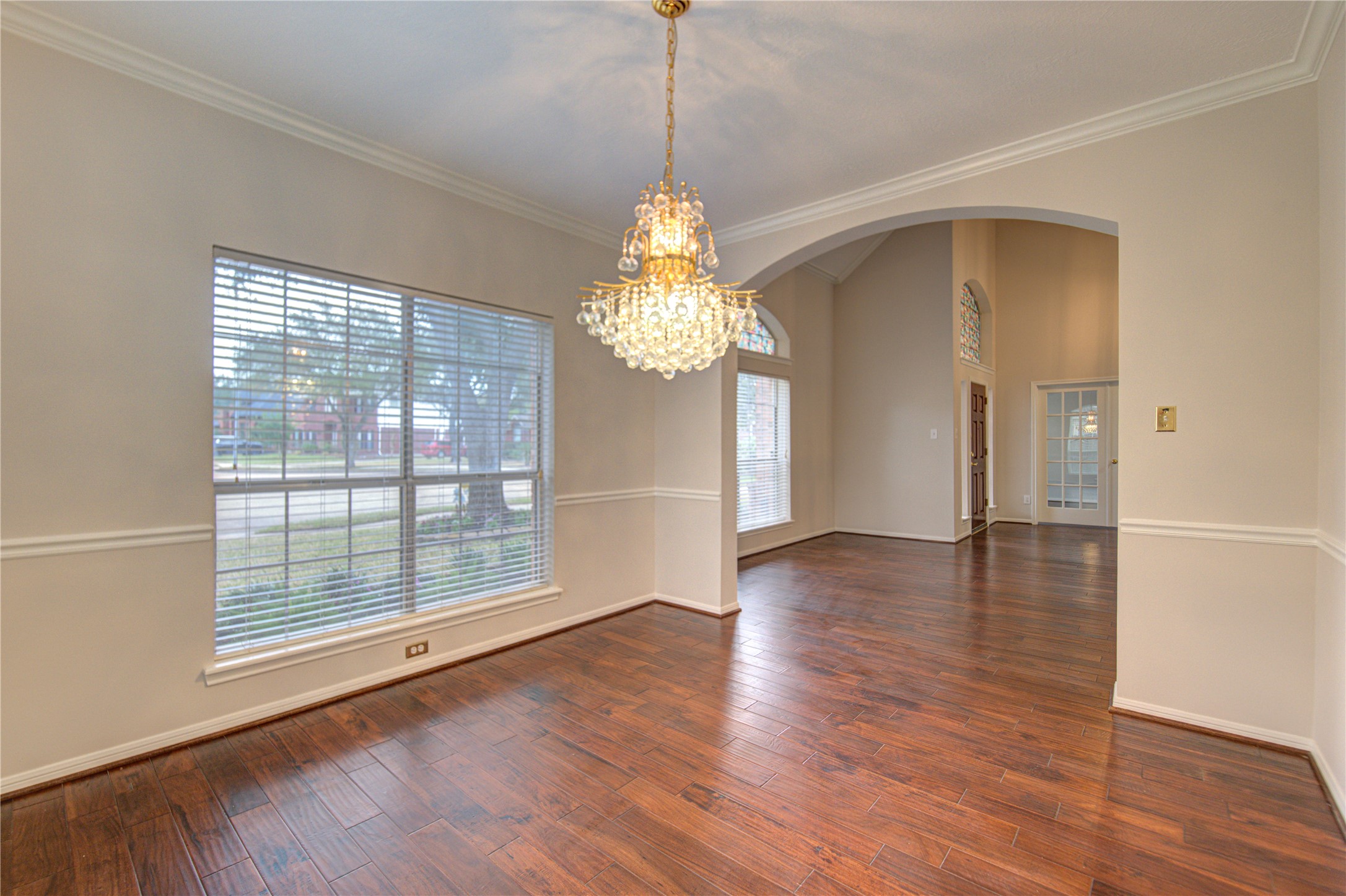 This room features elegant wood flooring, large windows with ample natural light, and a decorative chandelier, making it ideal for dining or a formal sitting area.