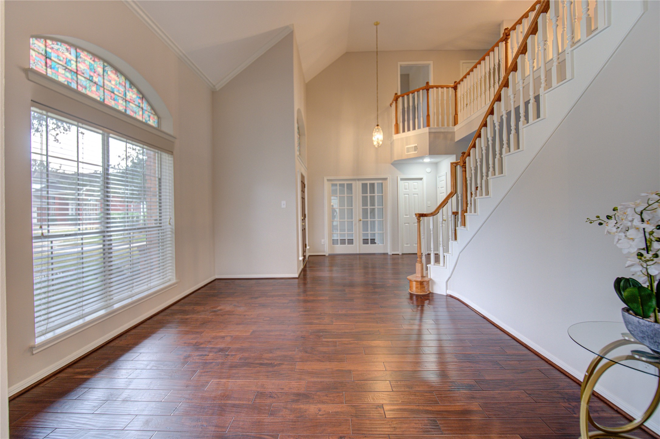 This spacious entryway features high ceilings, elegant hardwood floors, and abundant natural light from large windows. A grand staircase with wooden railing adds a touch of sophistication, and French doors lead to home office