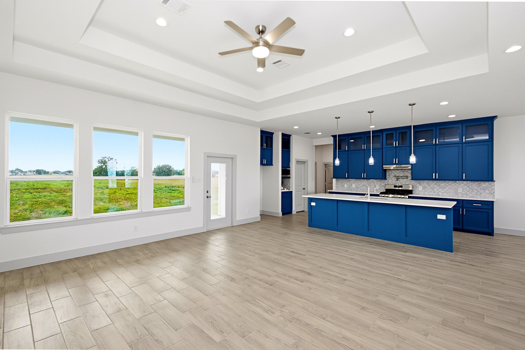 Spacious open-concept living area with elegant tile flooring, abundant natural light from large windows, and a striking kitchen featuring bold blue cabinetry and modern pendant lighting.