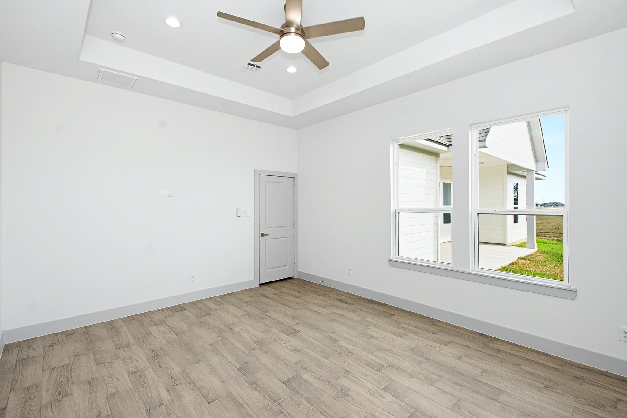 Bright and airy primary bedroom featuring a modern ceiling fan, wood-look tile flooring, and large windows overlooking a covered patio and expansive views.