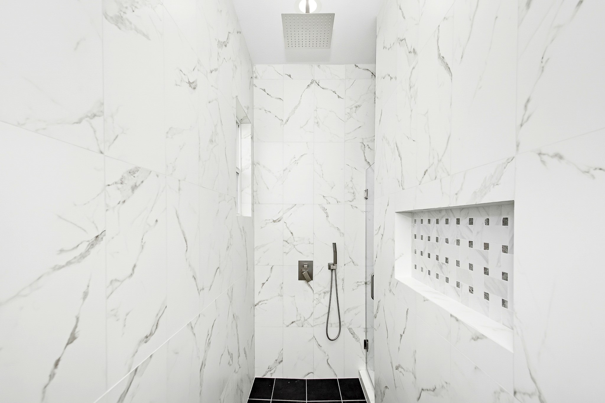 Luxurious shower with elegant marble walls, a sleek rainfall showerhead, and a modern recessed shelf for convenience.