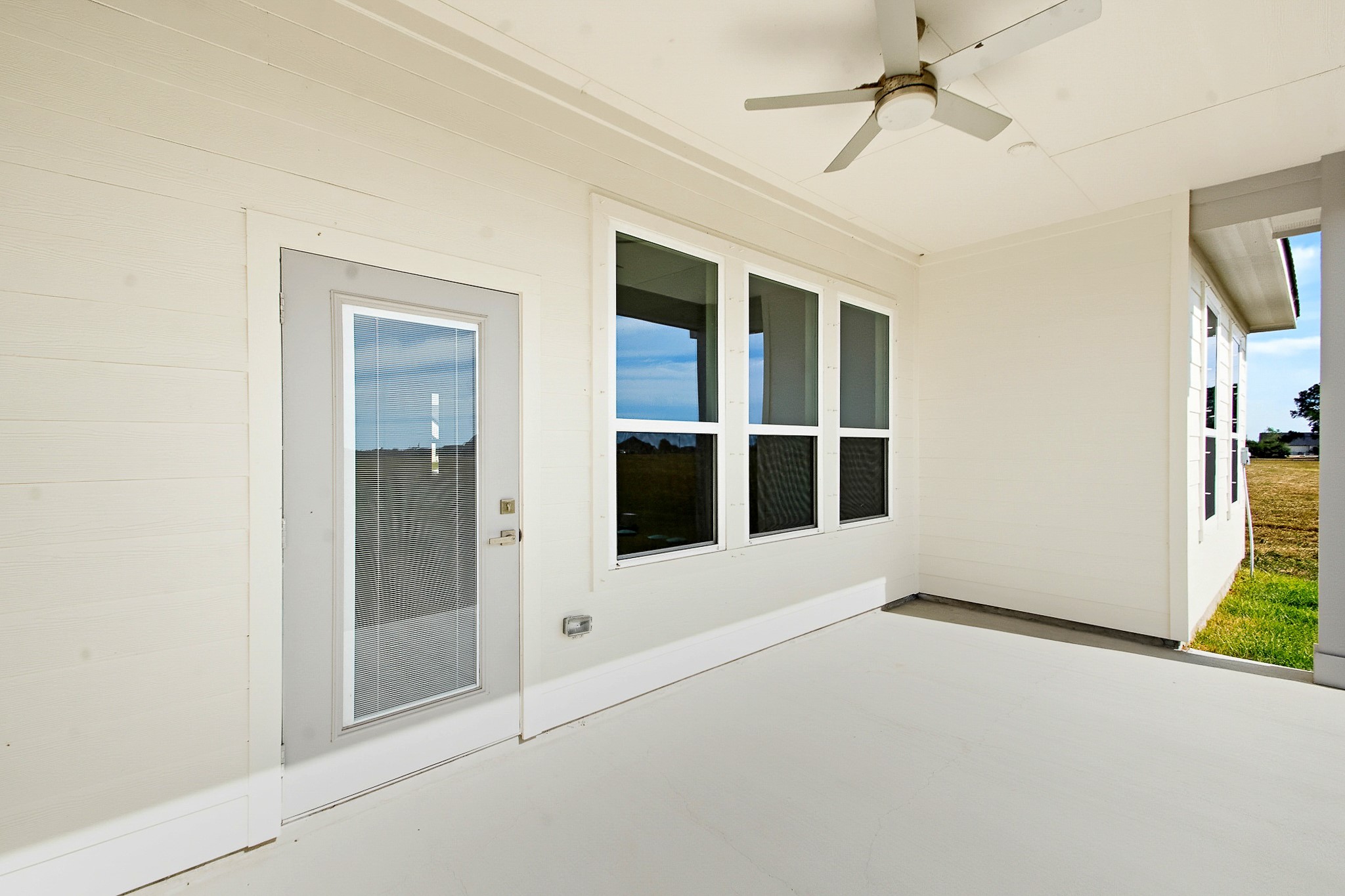 Spacious covered patio with modern ceiling fan and large windows, offering a seamless indoor-outdoor living experience with serene views. Situated on a 1 Acre lot.