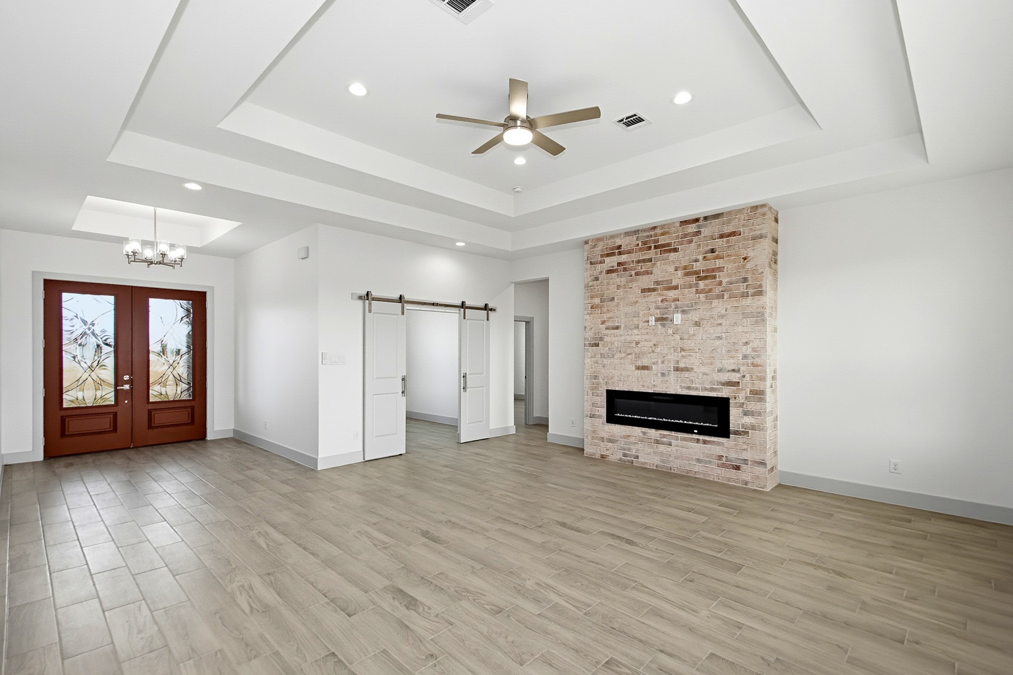 Elegant 19x 16 living area featuring a striking brick accent wall with a modern fireplace, complemented by stylish wood-look tile flooring and a chic coffered ceiling with recessed lighting.
