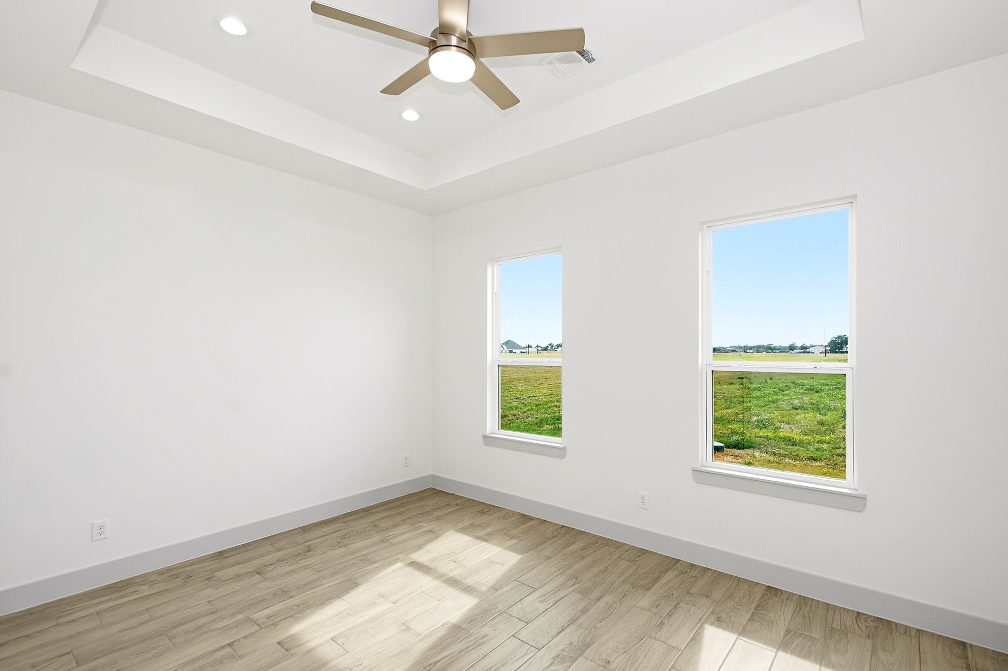 Bright 14.5x12 third bedroom with large windows offering scenic views, elegant tile flooring, and a modern ceiling fan set in a tray ceiling.