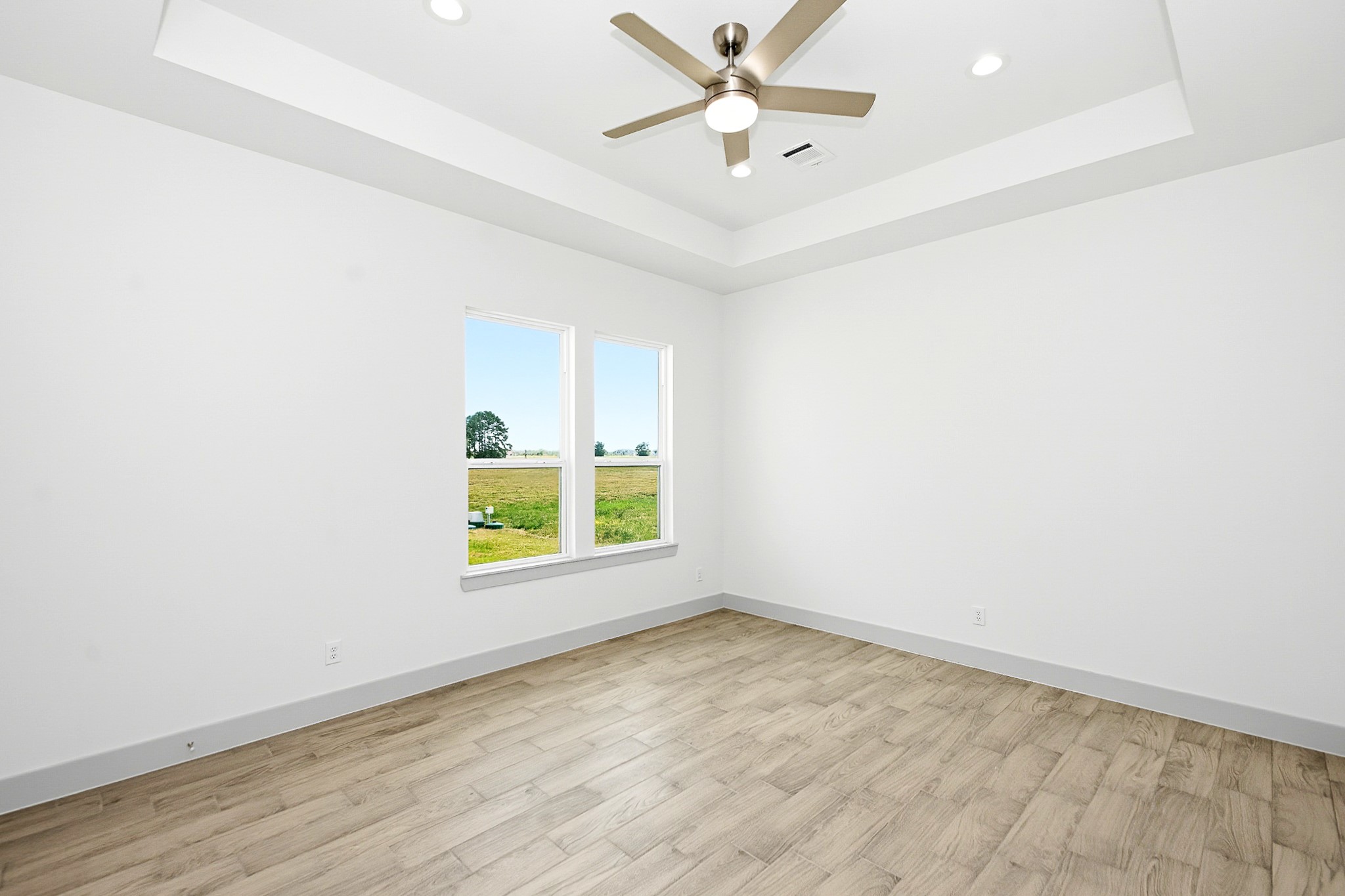 Bright and airy 16x13 Primary bedroom featuring a modern ceiling fan, elegant tray ceiling, and large windows offering scenic views.