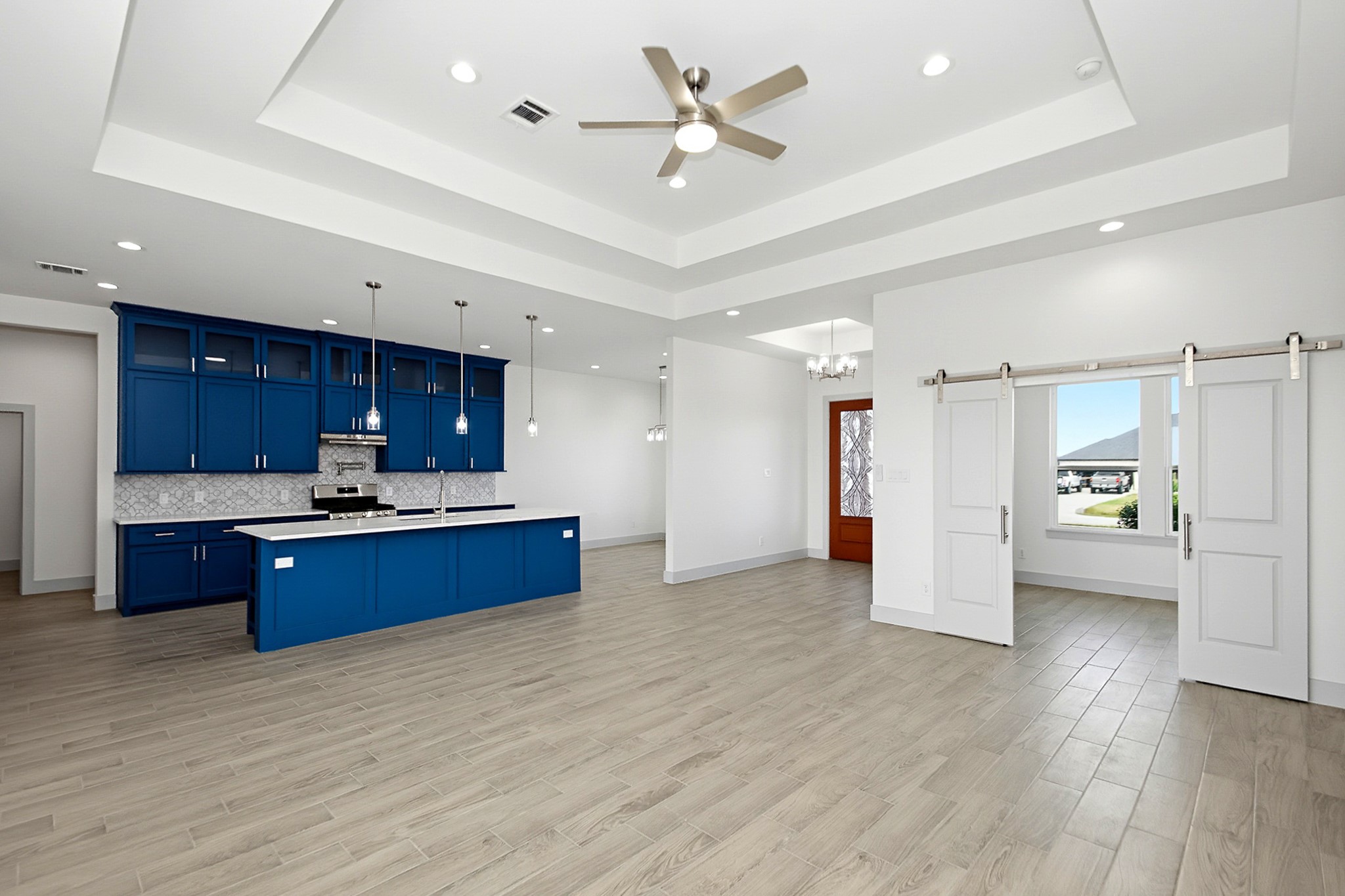 Spacious 19x16 open-concept living area featuring a modern kitchen with striking blue cabinetry, elegant pendant lighting, and a large center island, complemented by sleek flooring and stylish barn doors.