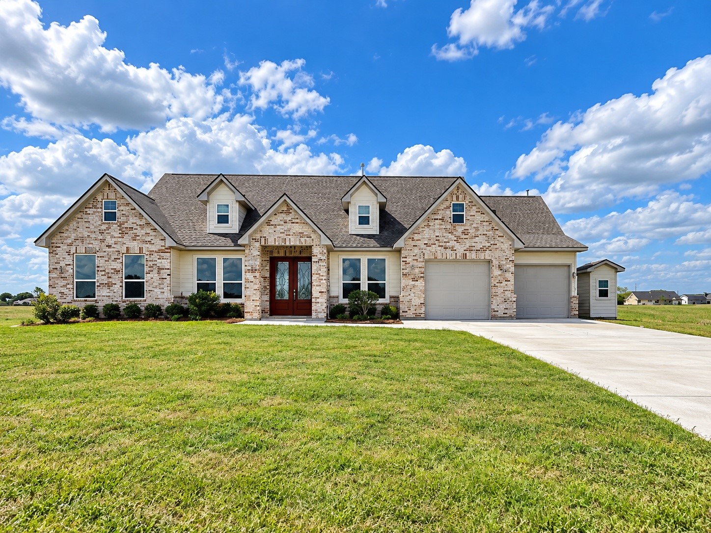 Charming 2389 sq.ft. brick home with a spacious double driveway, lush green lawn, and inviting double-door entry, set against a backdrop of blue skies and open fields.