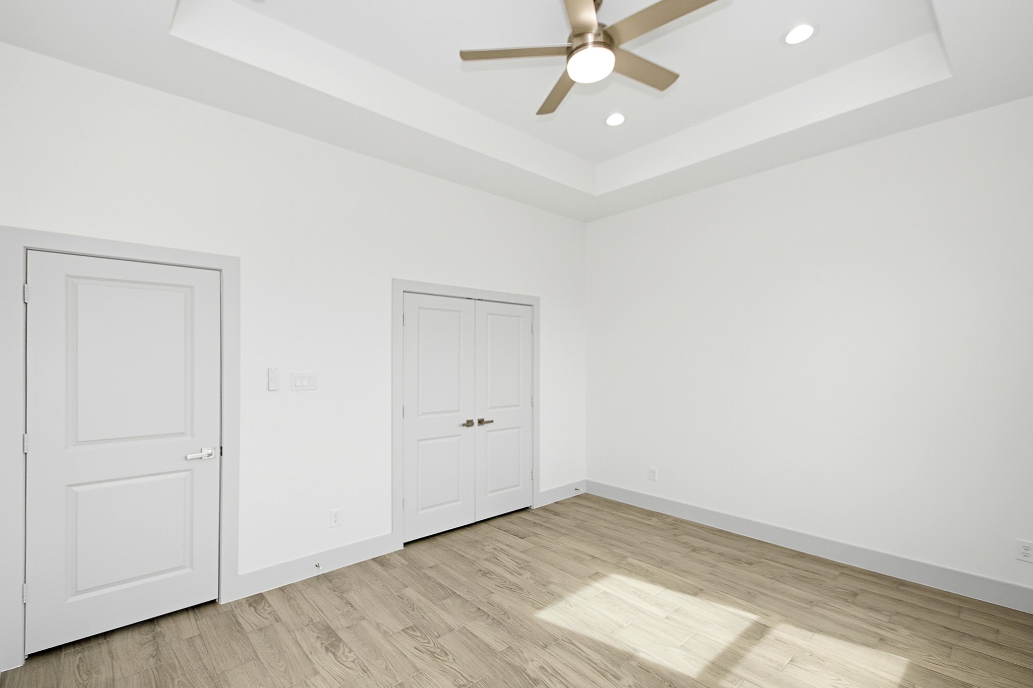 Bright and airy 14.5x12 third bedroom featuring sleek tile flooring, tray ceilings a modern ceiling fan, recessed lighting, double doors are the closet, offering a clean and contemporary space.
