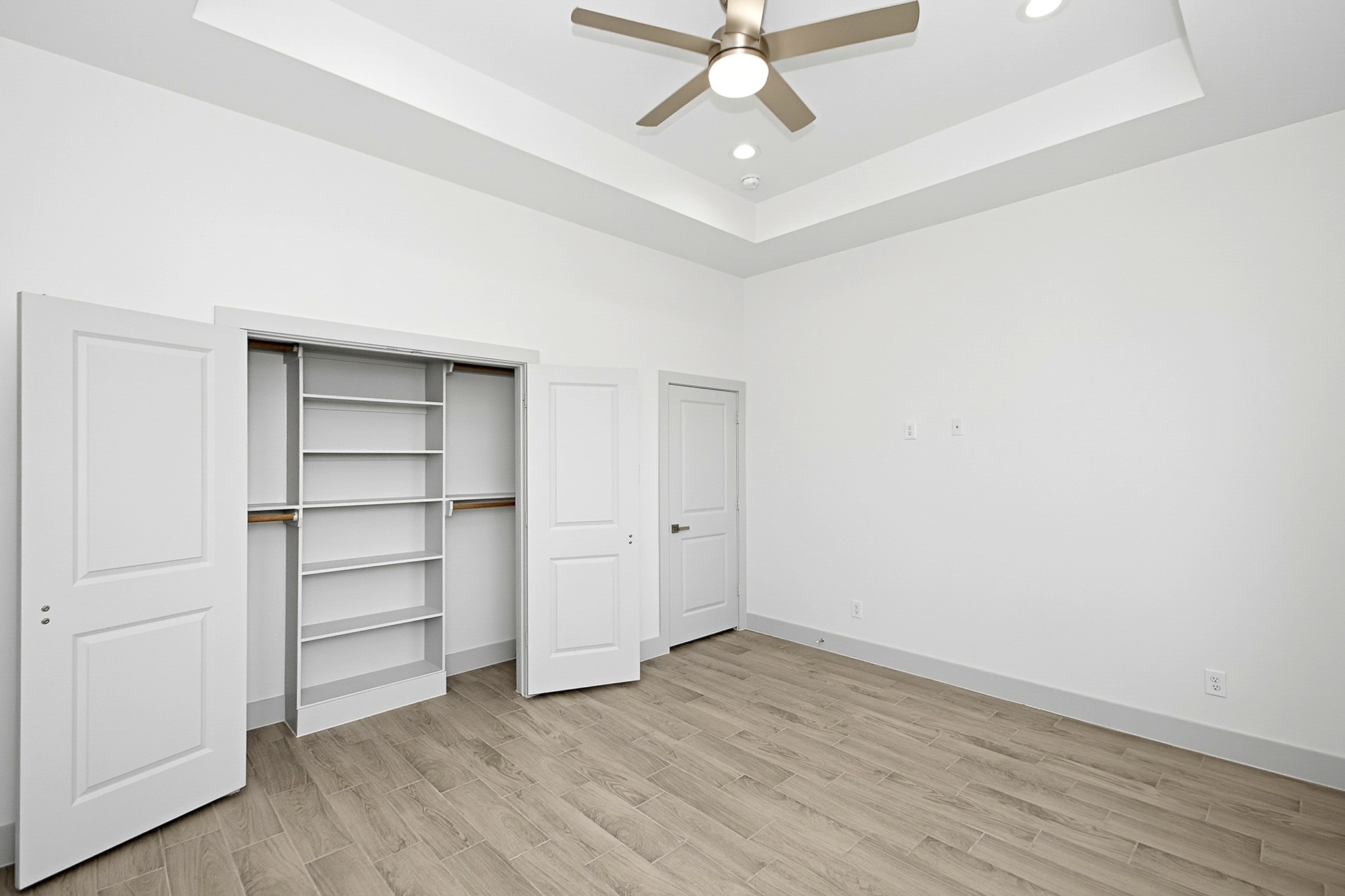 Spacious 14.5x12 bedroom featuring a tray ceiling, modern ceiling fan, and ample closet storage with built-in shelving.
