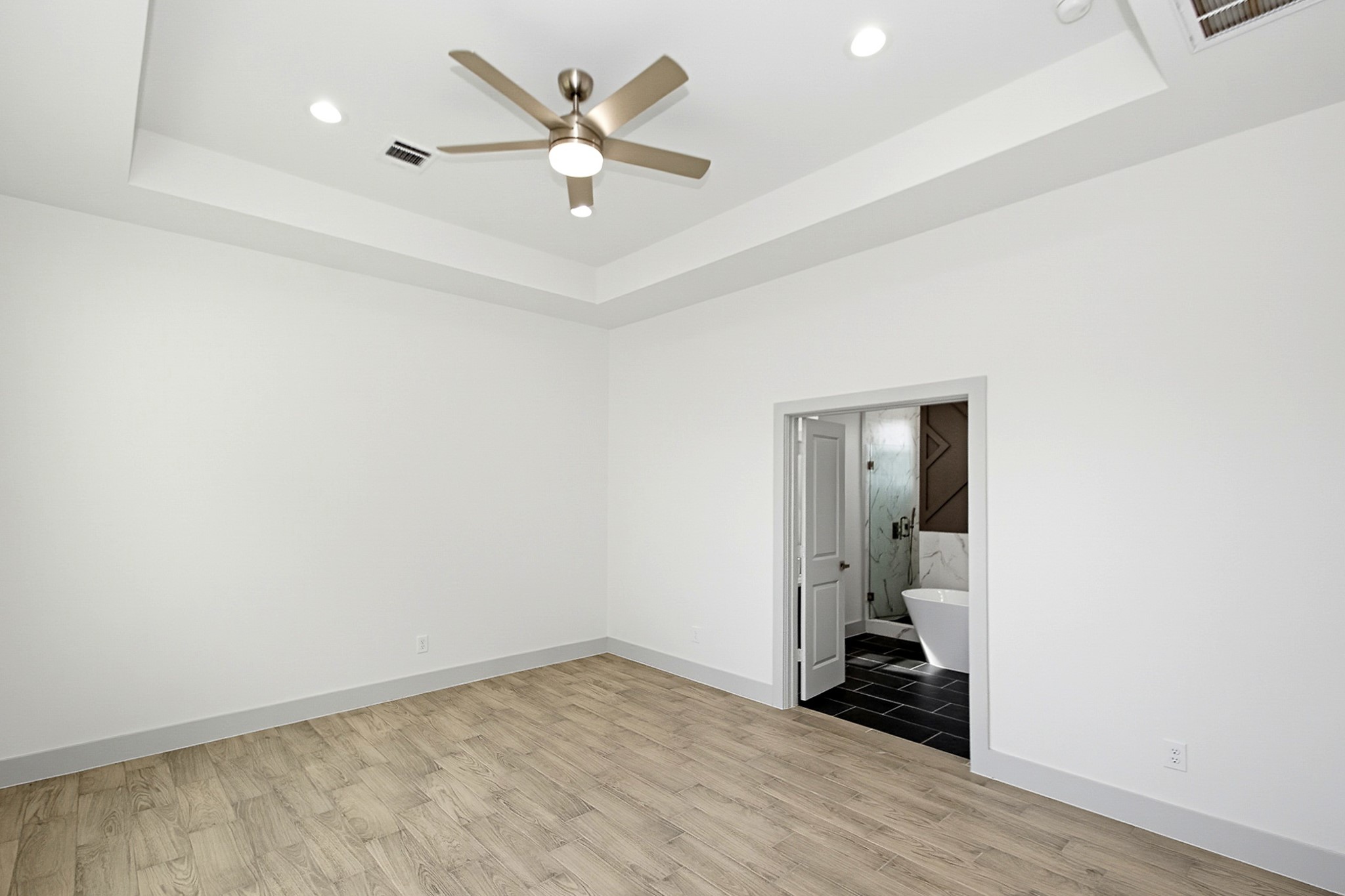 Spacious 16x13 Primary bedroom with elegant tile flooring, a modern ceiling fan, and recessed lighting, leading to a luxurious bathroom with a freestanding tub.
