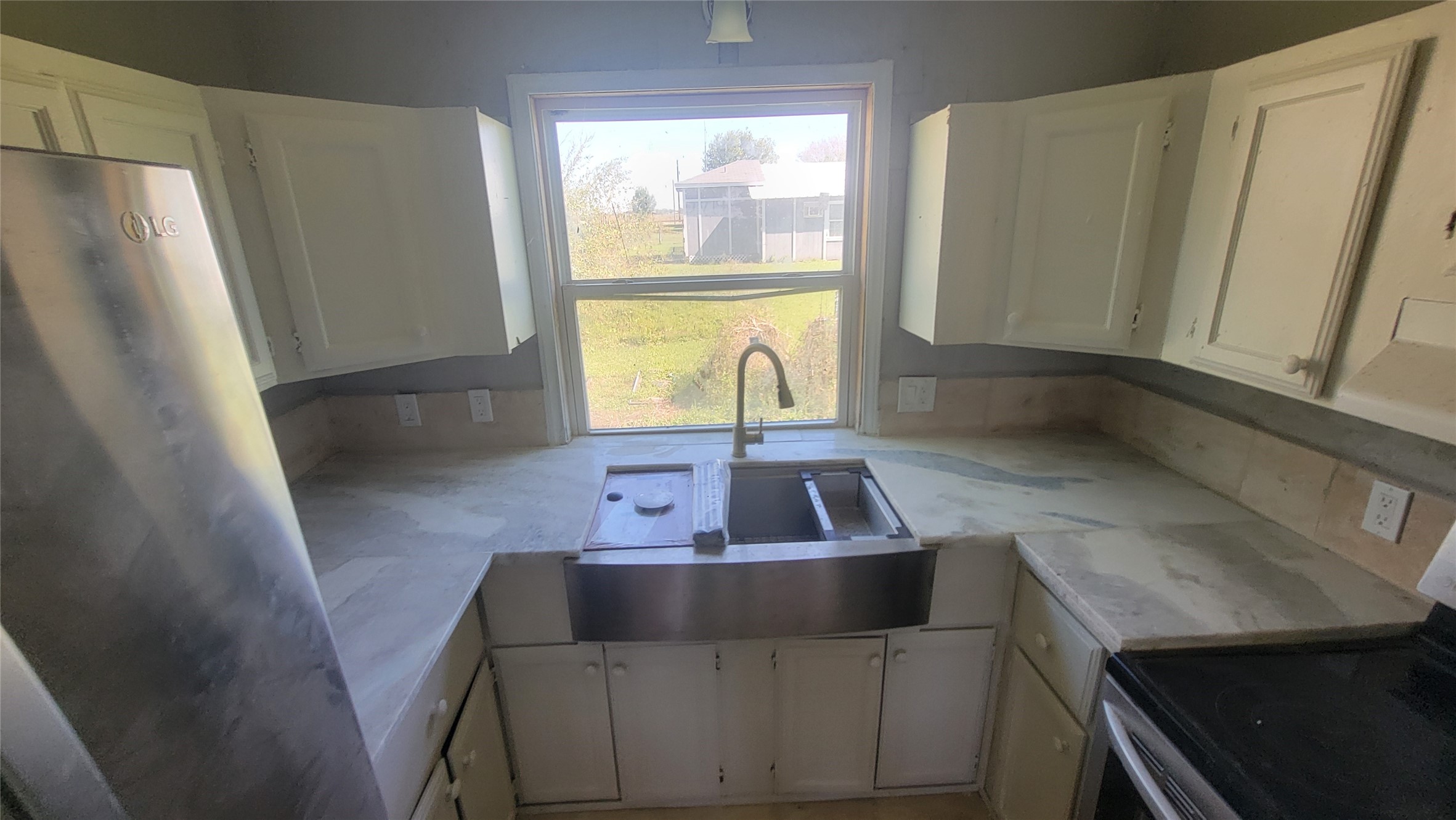 Cozy kitchen with natural light, featuring white cabinets, a farmhouse sink, and stainless steel appliances. Ideal for intimate cooking experiences with a view of the backyard.