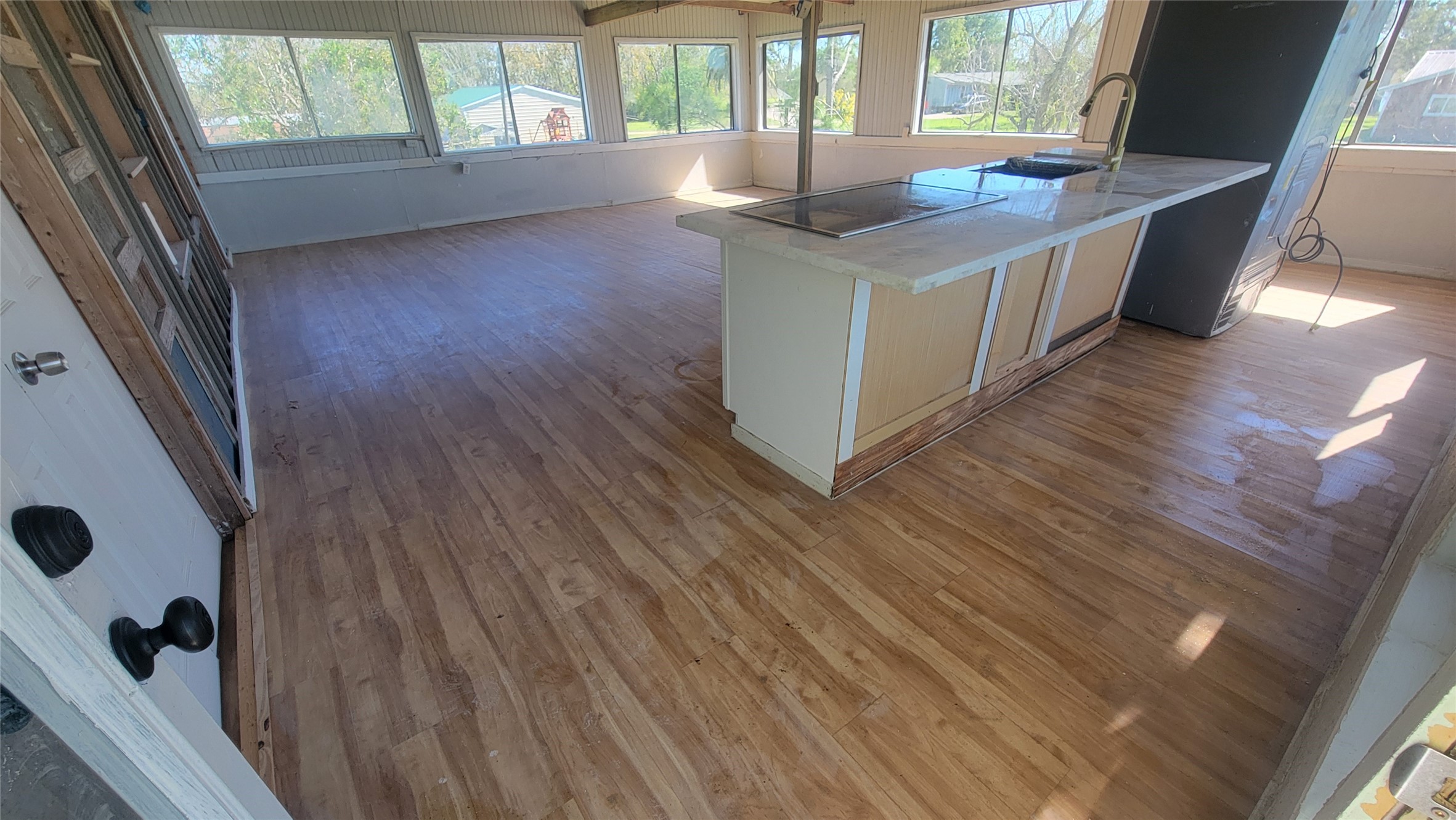 Spacious, sunlit kitchen with large windows, wood flooring, and a central island featuring a modern sink. Ideal for hosting and enjoying natural light.