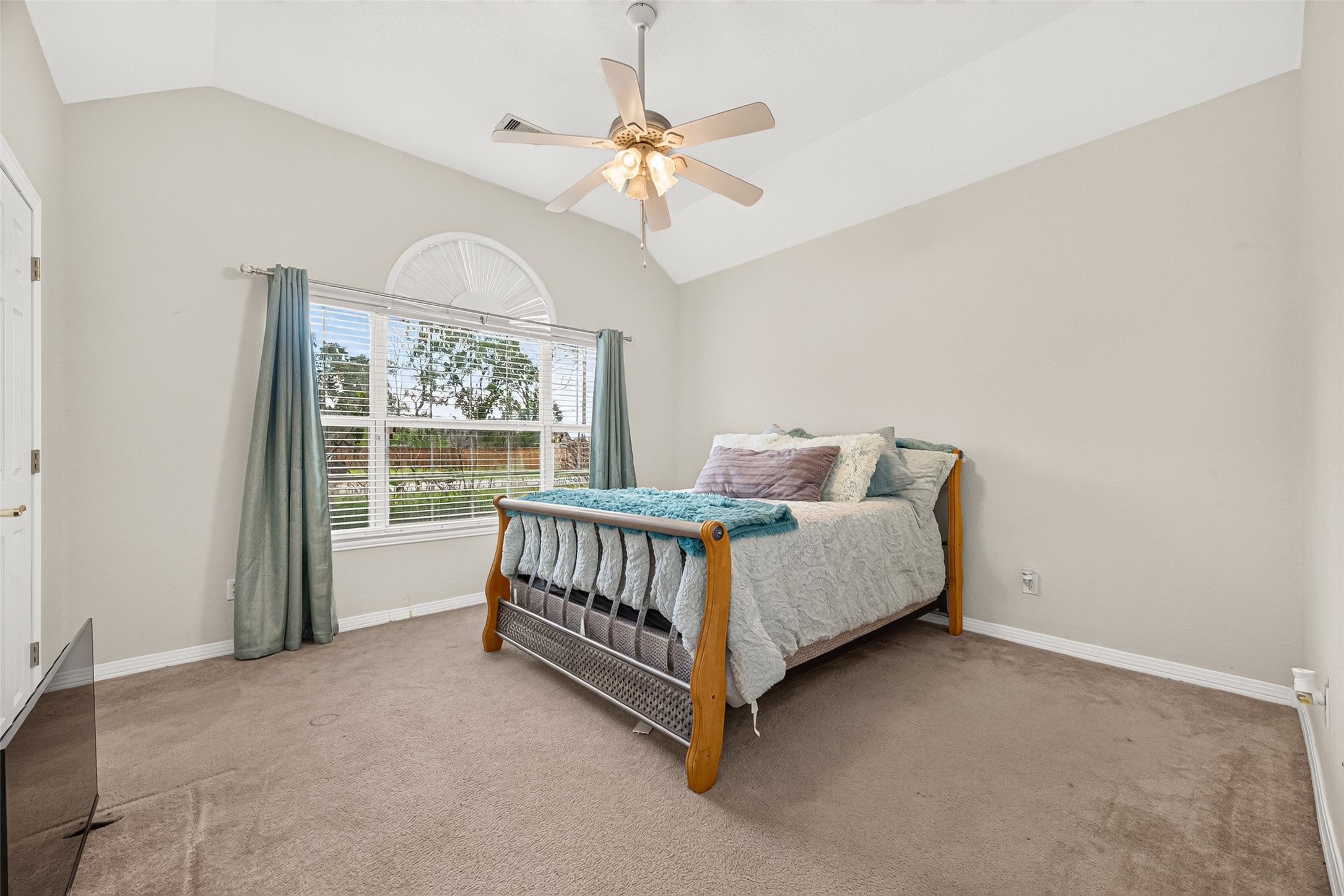 Spacious secondary bedroom featuring a vaulted ceiling, ceiling fan, and beautiful natural light from the large window.