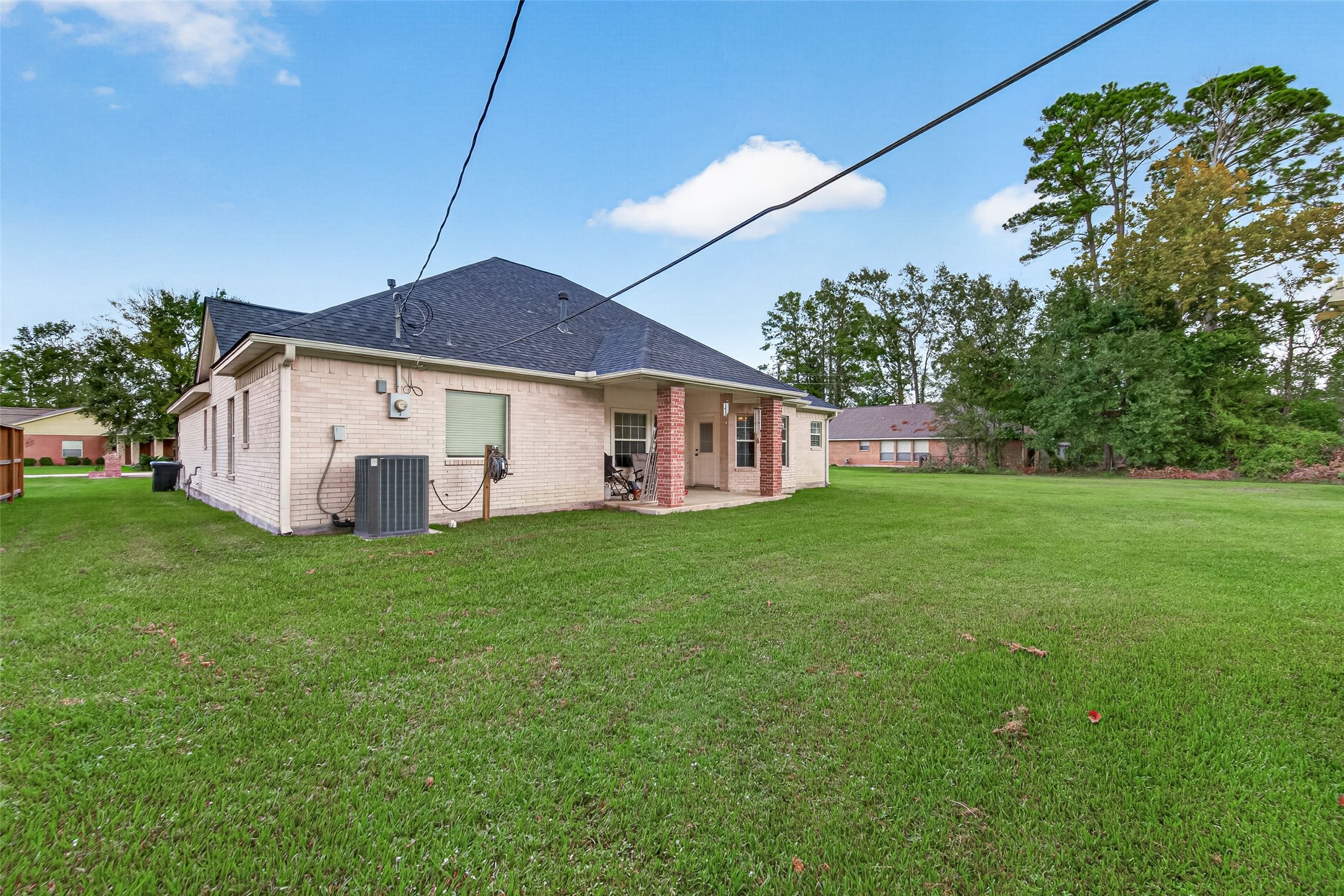 Beautiful rear view of the home showcasing the covered patio, brick exterior, and generous backyard with plenty of open green space.