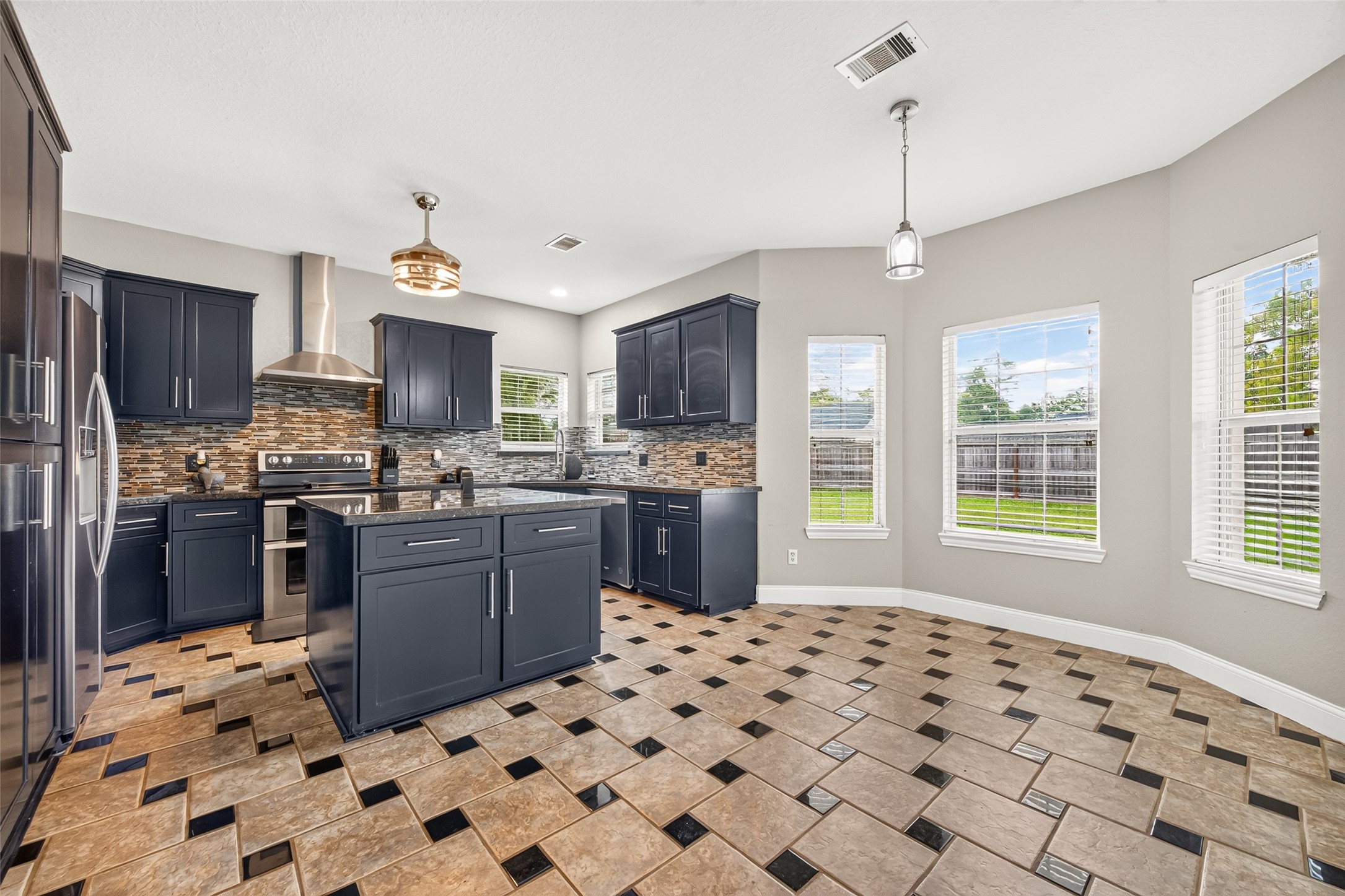 Spacious kitchen featuring rich dark cabinetry, a center island, stainless steel appliances, and a bright breakfast area surrounded by windows.