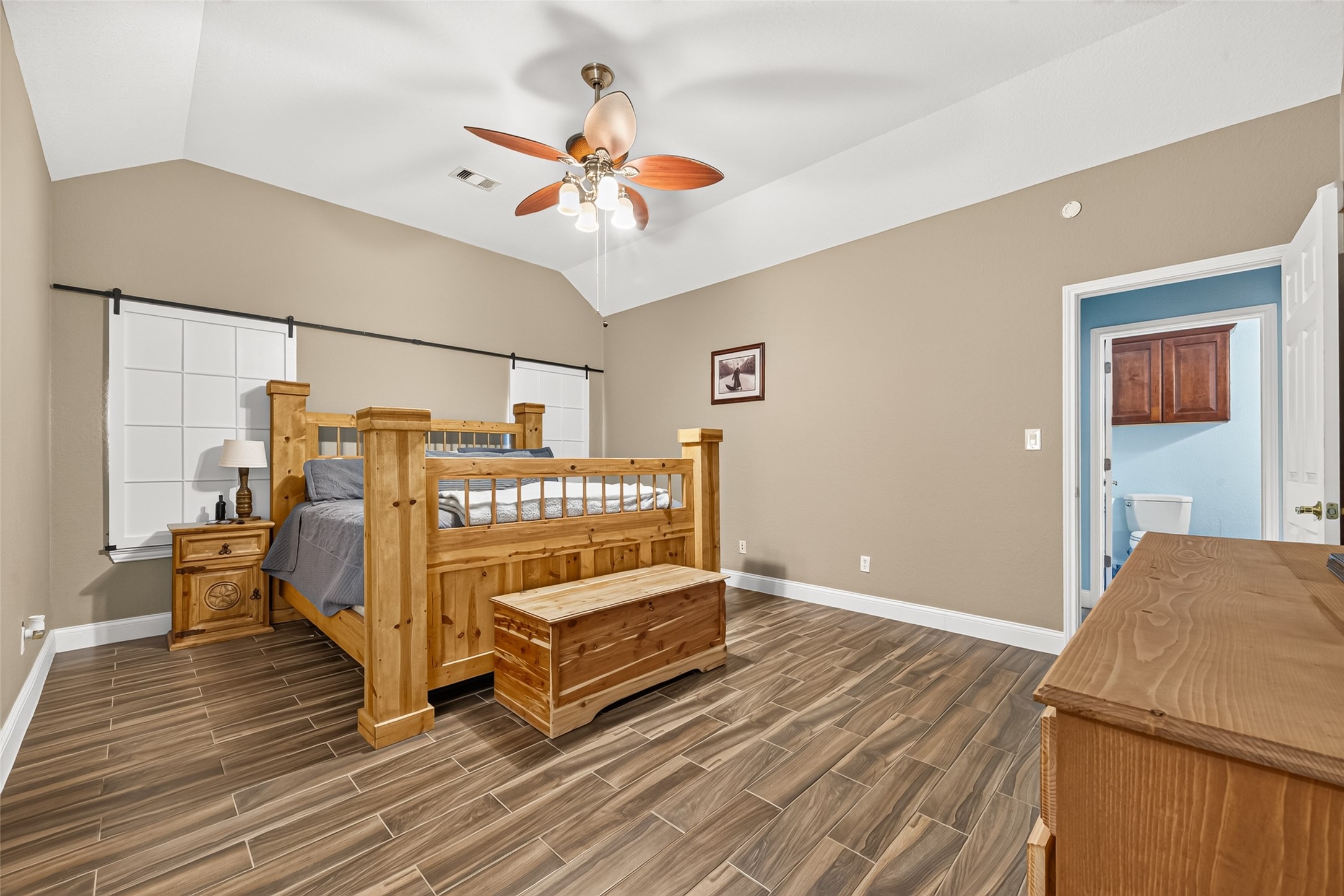Another view of the inviting primary suite showcasing its generous layout, ceiling fan, and beautiful flooring.