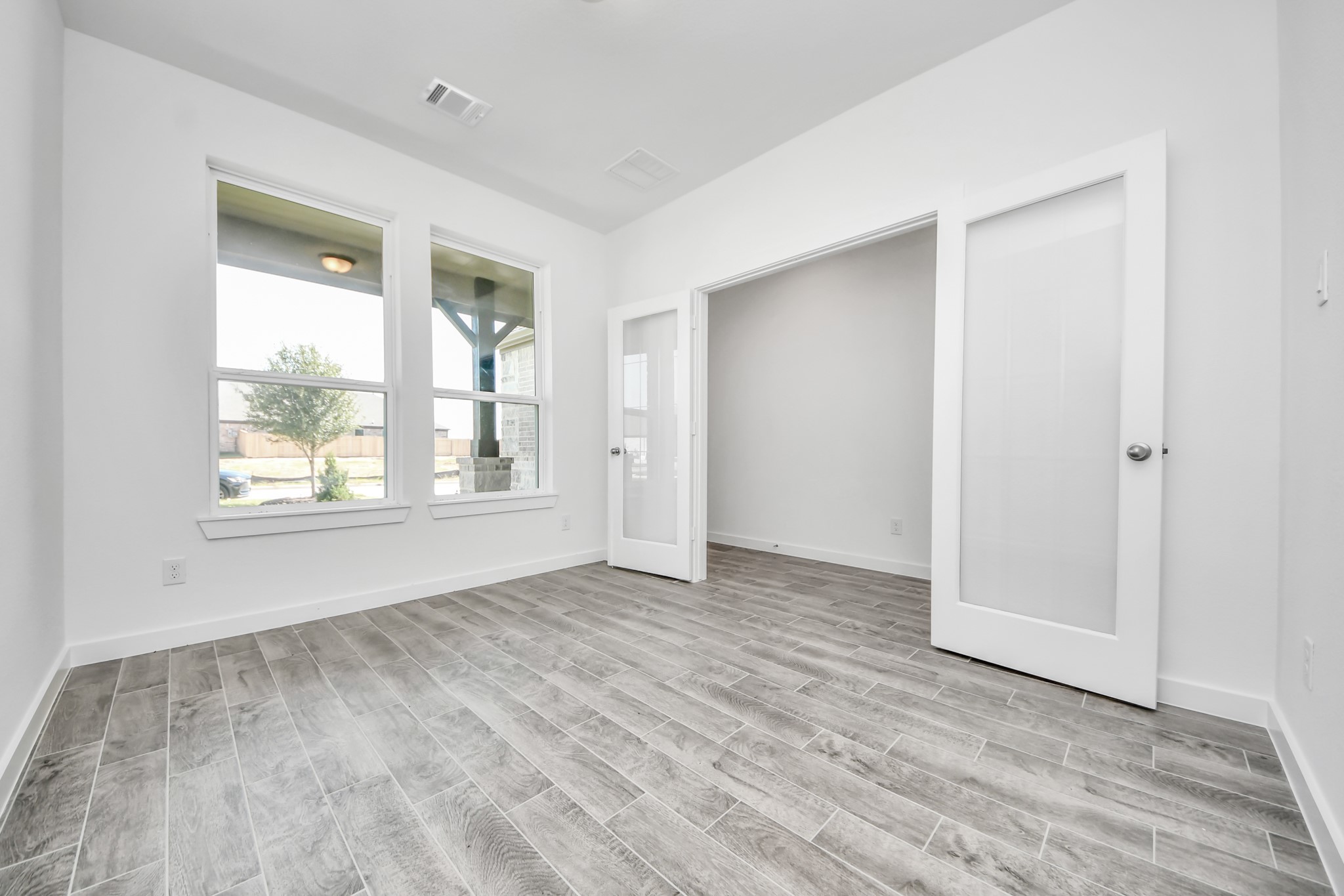 Experience the perfect blend of sophistication and warmth in this home office, boasting elegant wood-look tile flooring and flooded with natural light from expansive windows and French doors.