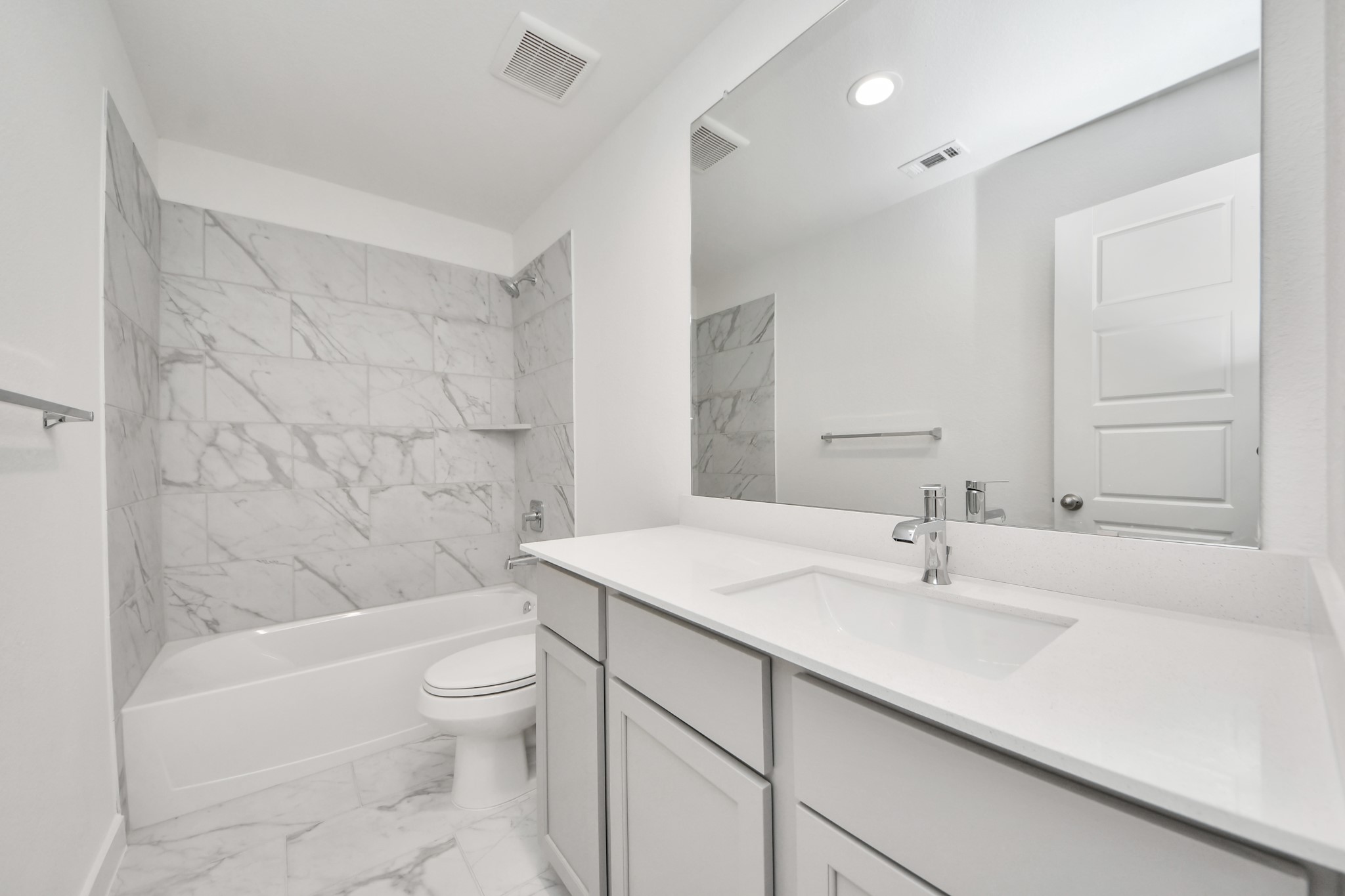 Secondary bath features tile flooring, bath/shower combo with tile surround, light stained wood cabinets, beautiful light countertop.