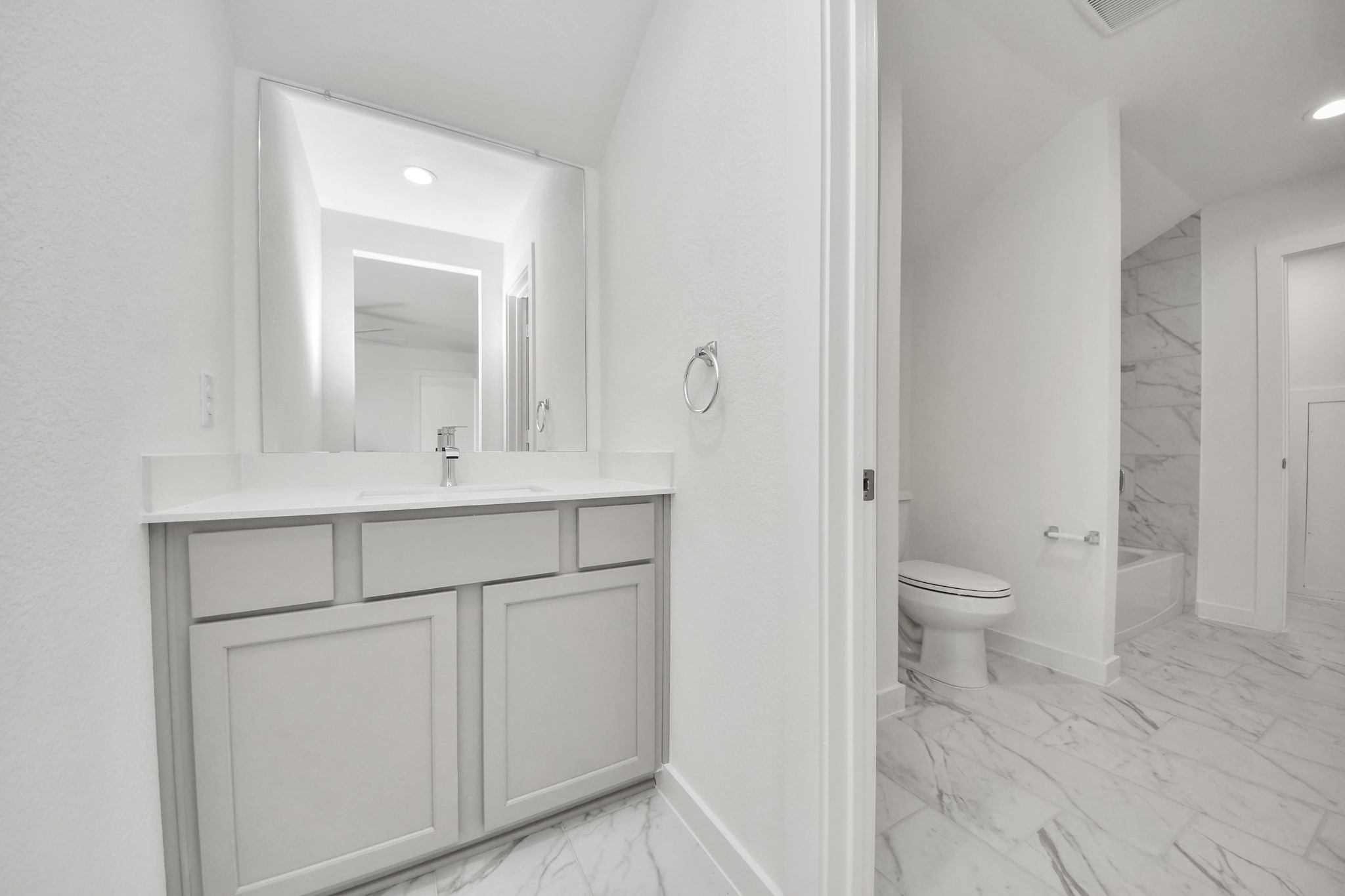 Experience convenience in the secondary bathroom, designed for Jack and Jill arrangements, now with a separate vanity area. This well-appointed space showcases stylish tile flooring, a bath/shower combo with an elegant tile surround, and light-stained wood cabinets. The beautiful light countertop adds a touch of sophistication, combining functionality and aesthetics seamlessly.