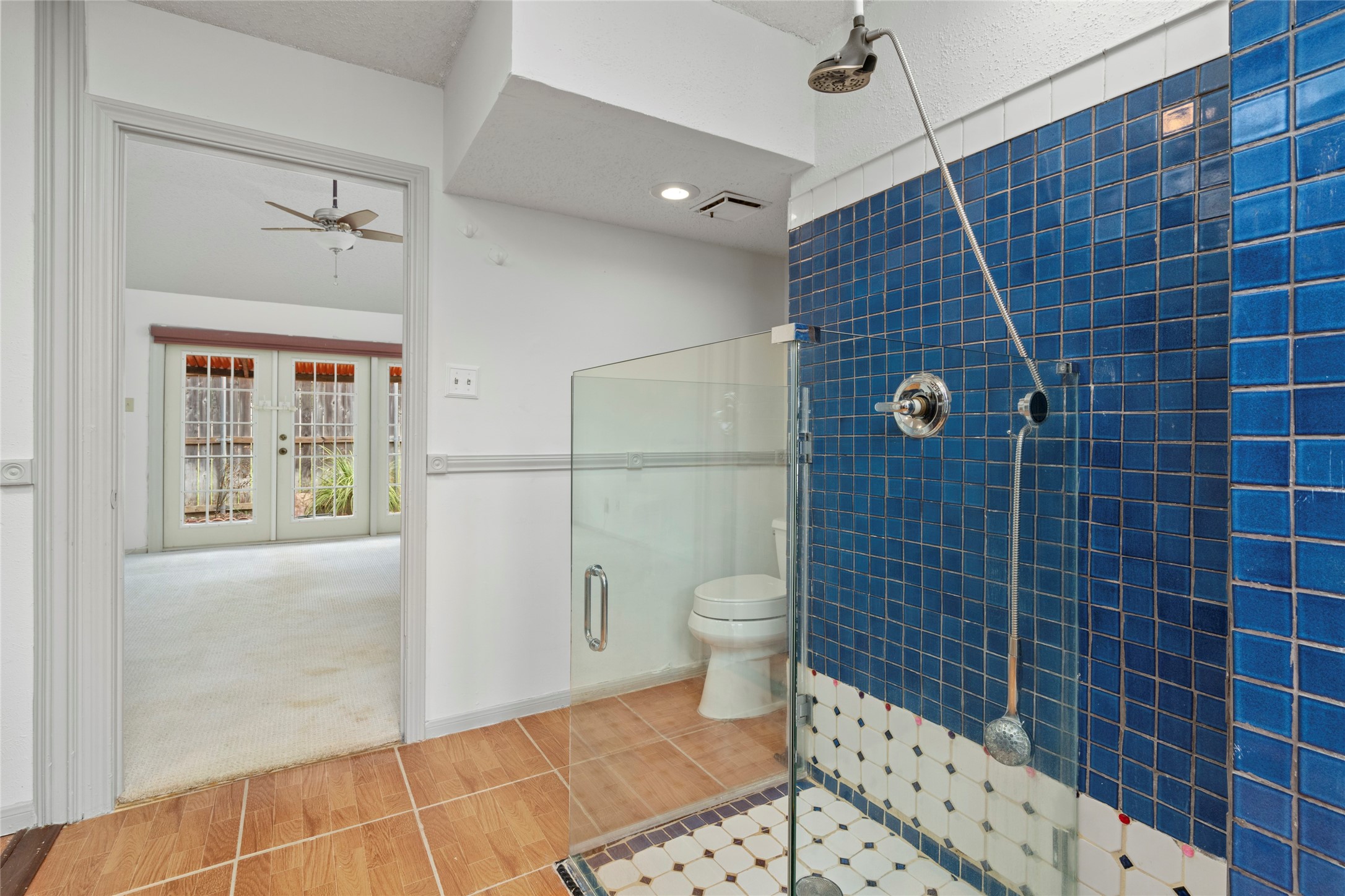 Primary bathroom featuring a striking blue-tiled shower, adding a spa-like touch of color and texture to the space.