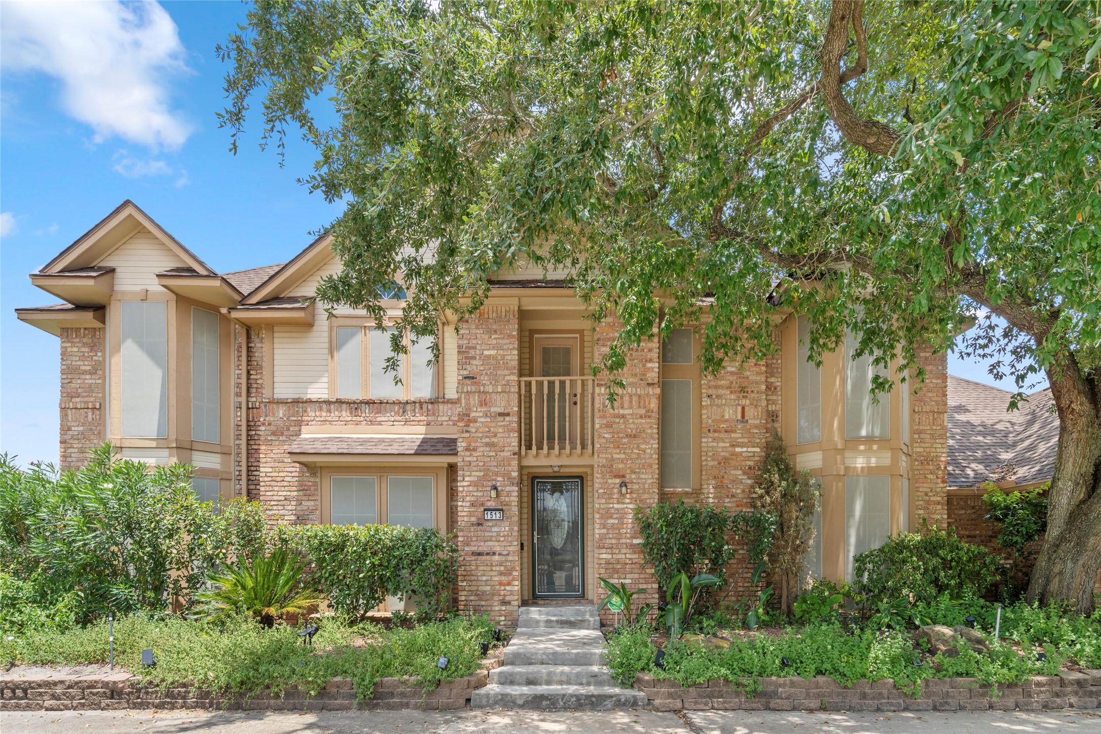 A daytime front exterior view highlighting the home's classic brick faade, mature landscaping, and inviting two-story silhouette.