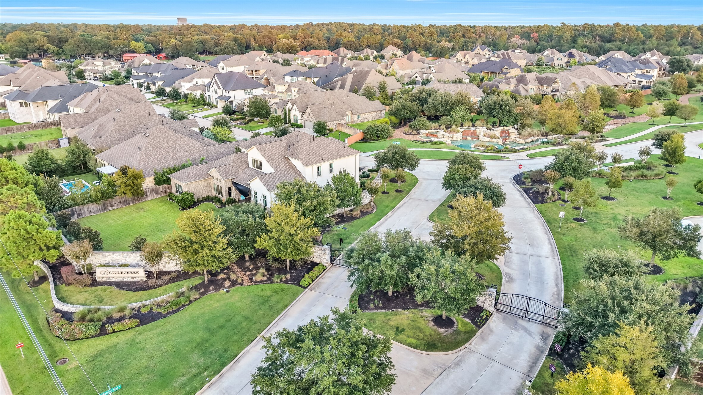 This aerial view captures the gated entrance to the community, with manicured medians and mature trees lining the drive  setting the tone for the quiet, private neighborhood beyond.
