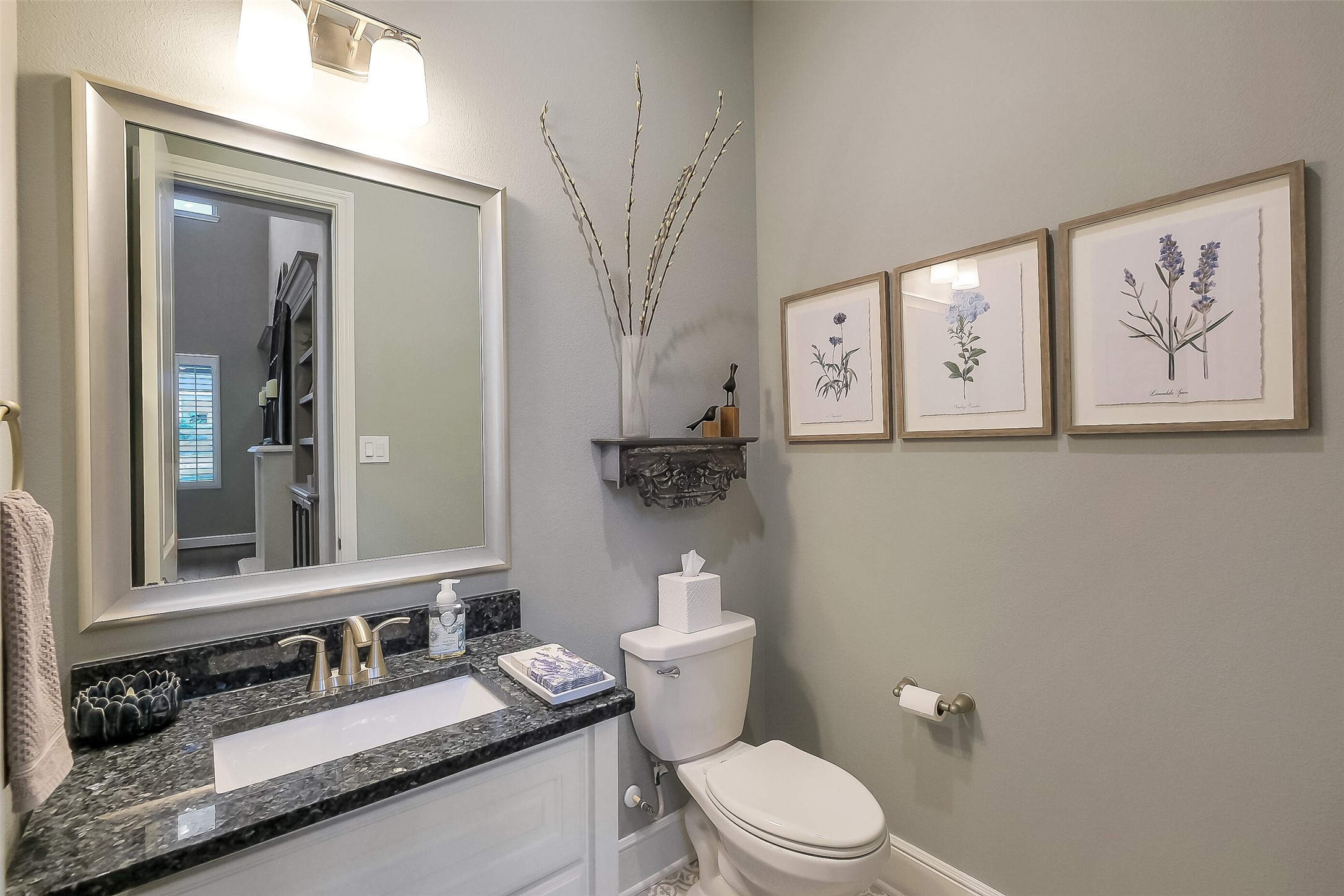 The first floor powder bathroom features granite counters, framed mirror and trending floor tile