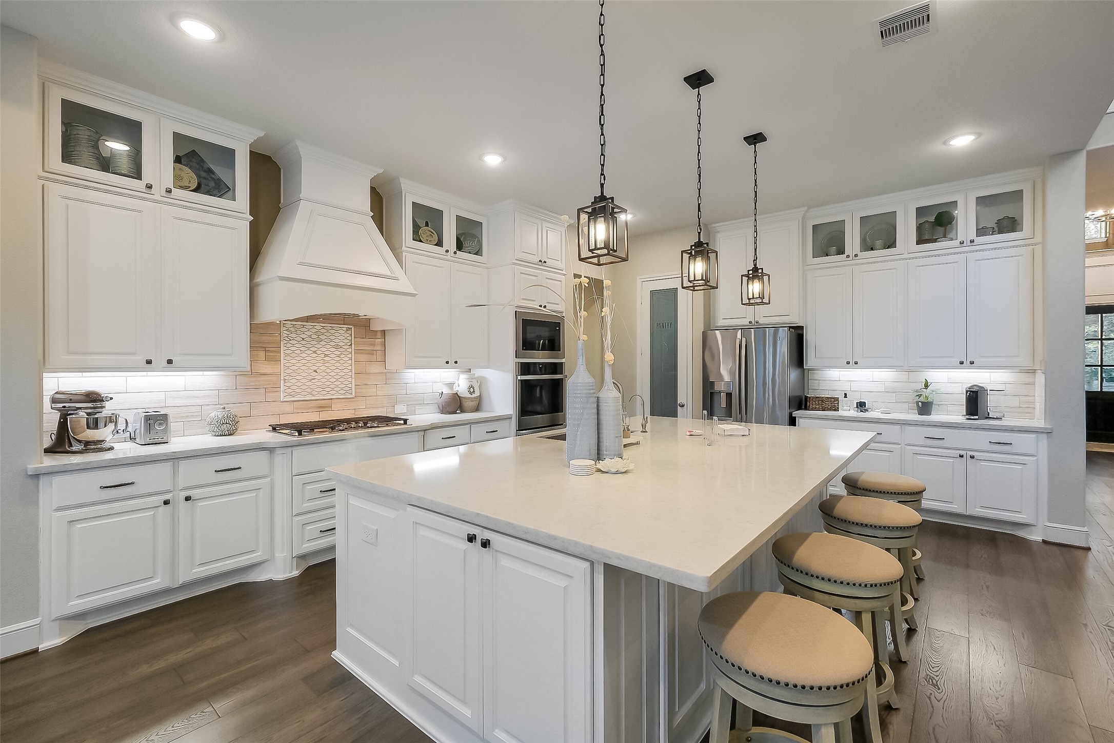 This bright white kitchen is built for both everyday living and entertaining, with a large quartz island, designer pendant lighting, and glass-front cabinetry that extends to the ceiling. The walk in pantry and storage under the island ensure you have storage for all of your cooking and This bright white kitchen is built for both everyday living and entertaining, with a large quartz island, designer pendant lighting, and glass-front cabinetry that extends to the ceiling. The walk in pantry and storage under the island ensure you have storage for all of your cooking and