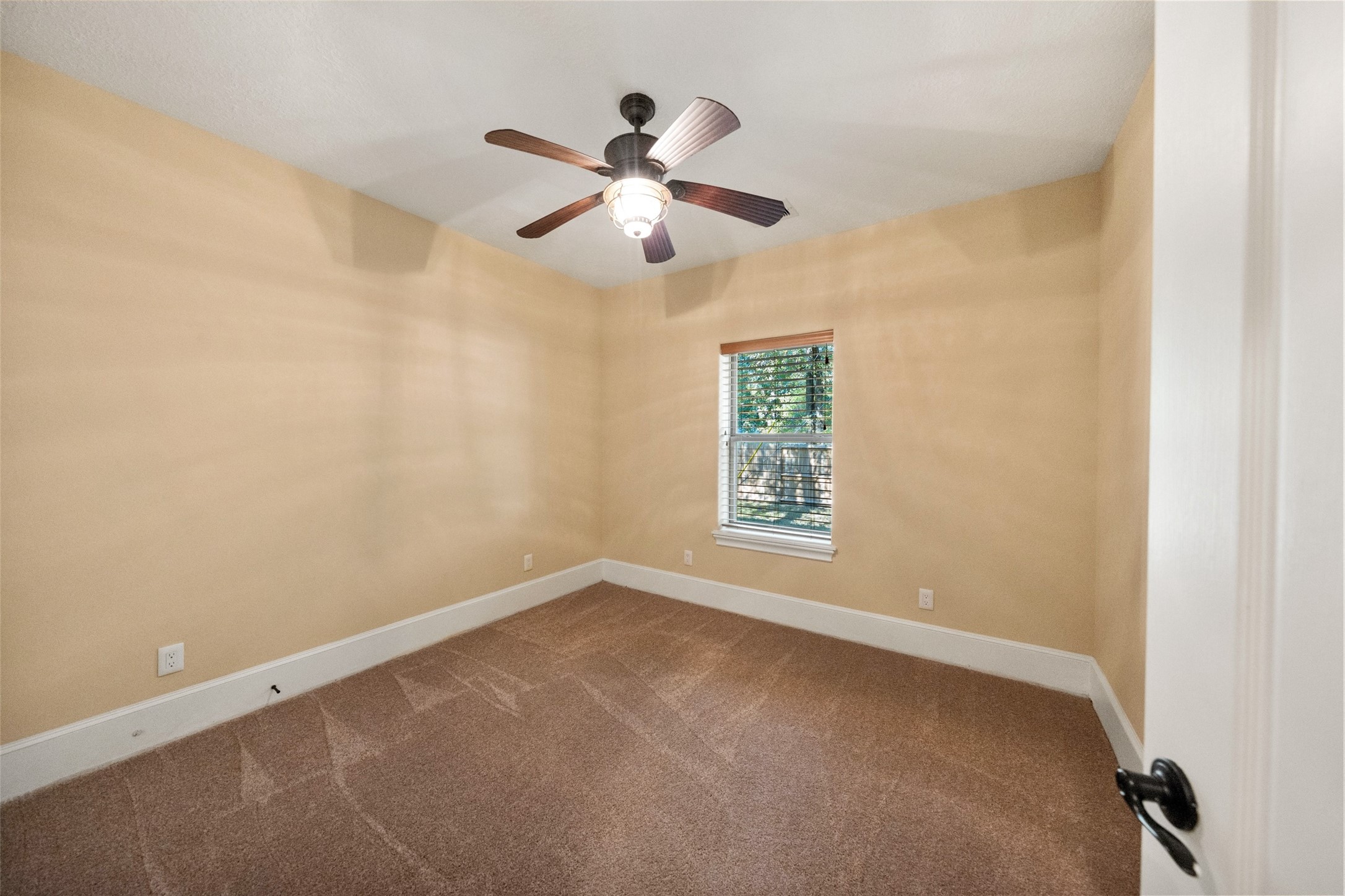 Cozy guest bedroom with soft natural light and a ceiling fan, perfect for relaxation.