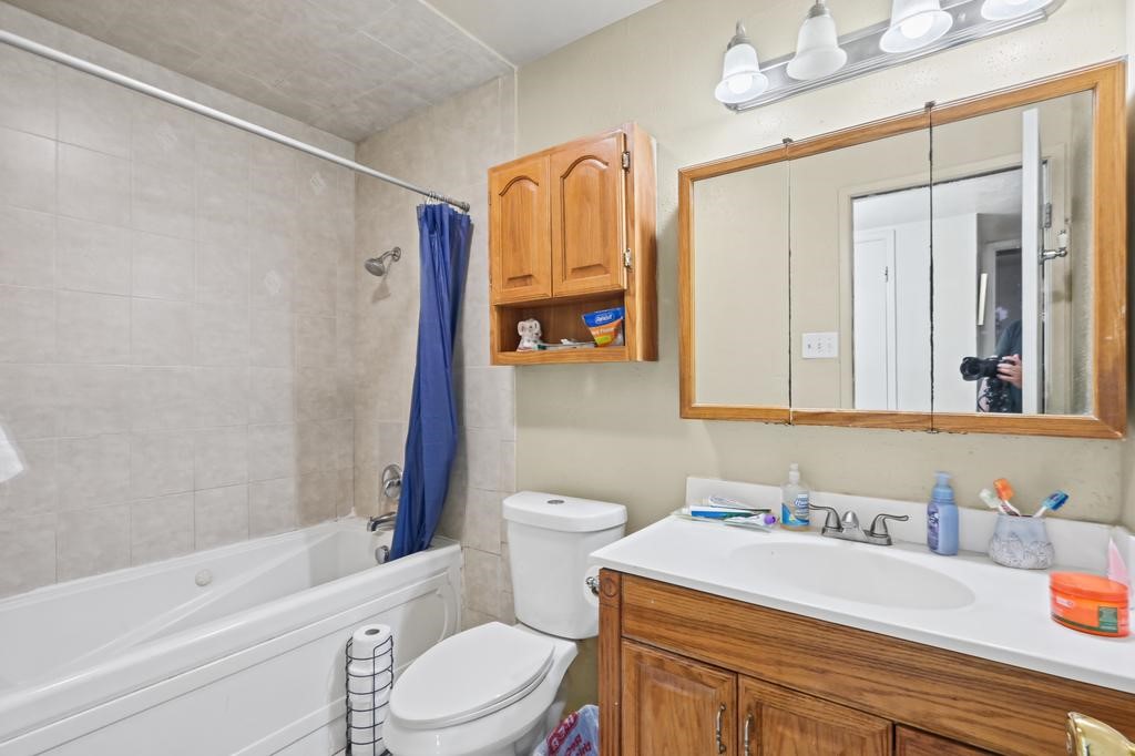 Bathroom featuring a spacious tub,  tilework, and ample storage with a wooden vanity and overhead cabinet for a cozy, functional space.
