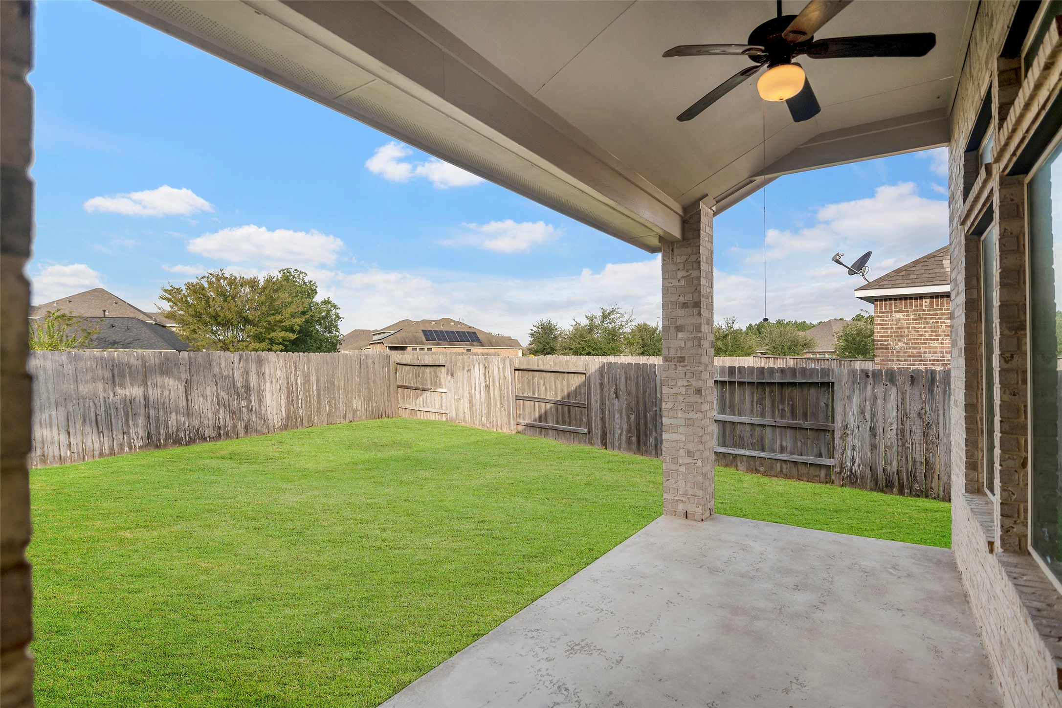 Charming covered patio with ceiling fan overlooks a spacious, fenced backyard, perfect for outdoor relaxation and entertaining.