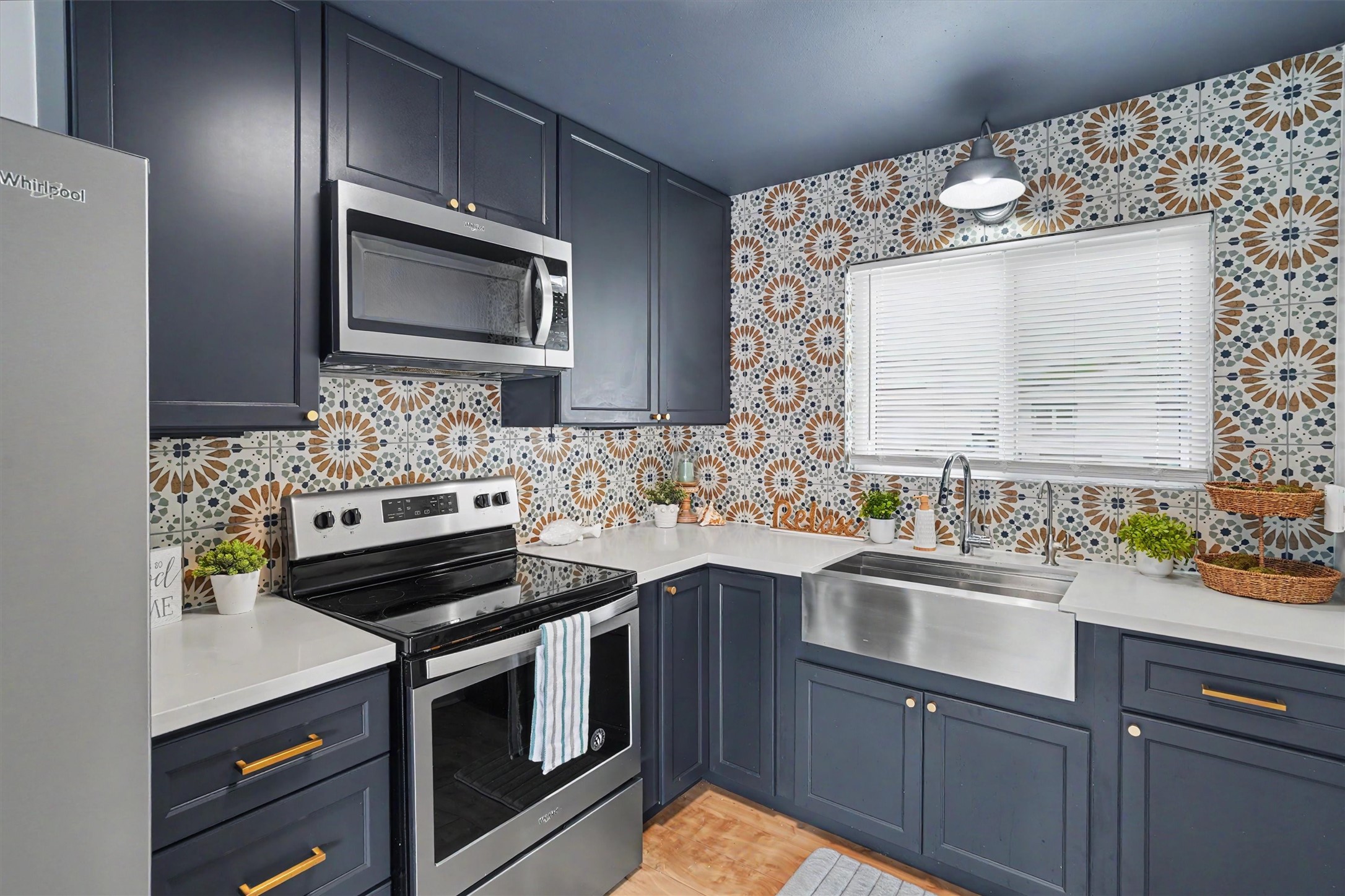 This modern kitchen is stylish with updated cabinets and brushed gold hardware, stainless appliances and farm sink, a featured kitchen wall with tile to the ceiling, and quartz countertops
