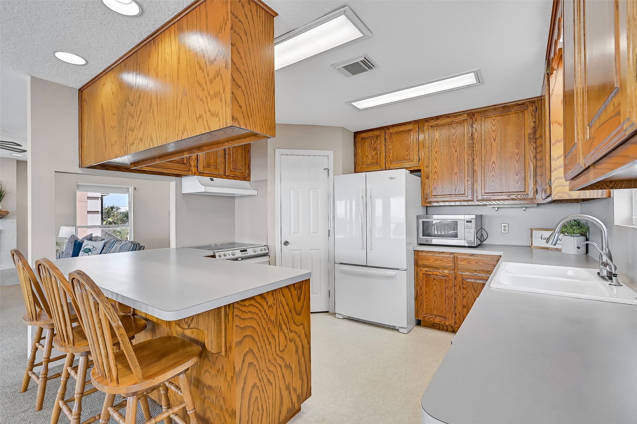 The kitchen offers generous workspace, abundant oak cabinetry, a breakfast bar for casual seating, and a functional layout that opens directly to the living and dining areas. Whether preparing dinner or morning coffee, the bay remains just steps away.